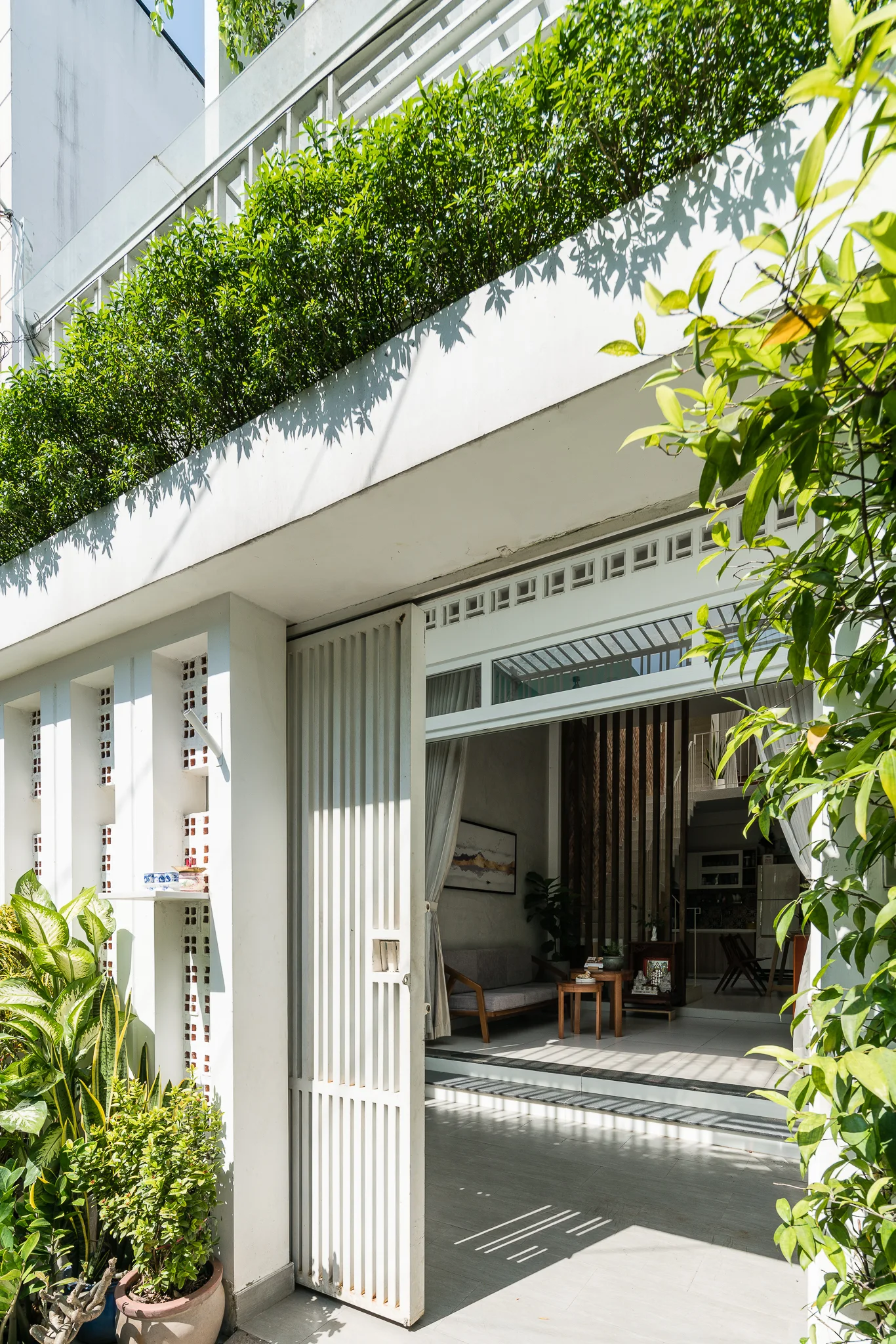 A modern white house entrance featuring an open slatted sliding gate, a breeze block wall, and potted green plants.