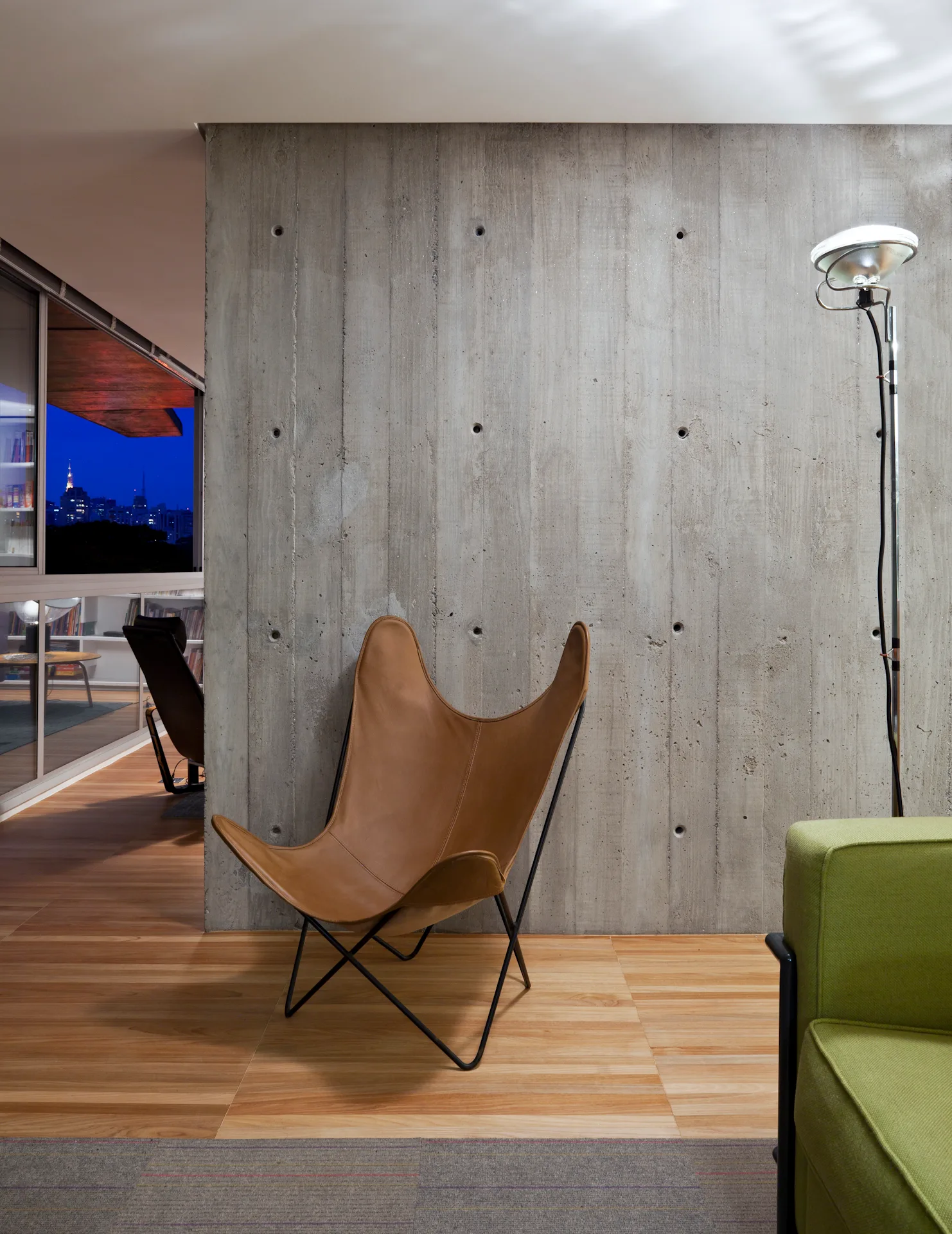 A tan leather butterfly chair sits in front of a textured concrete accent wall on wood flooring in a modern living space.