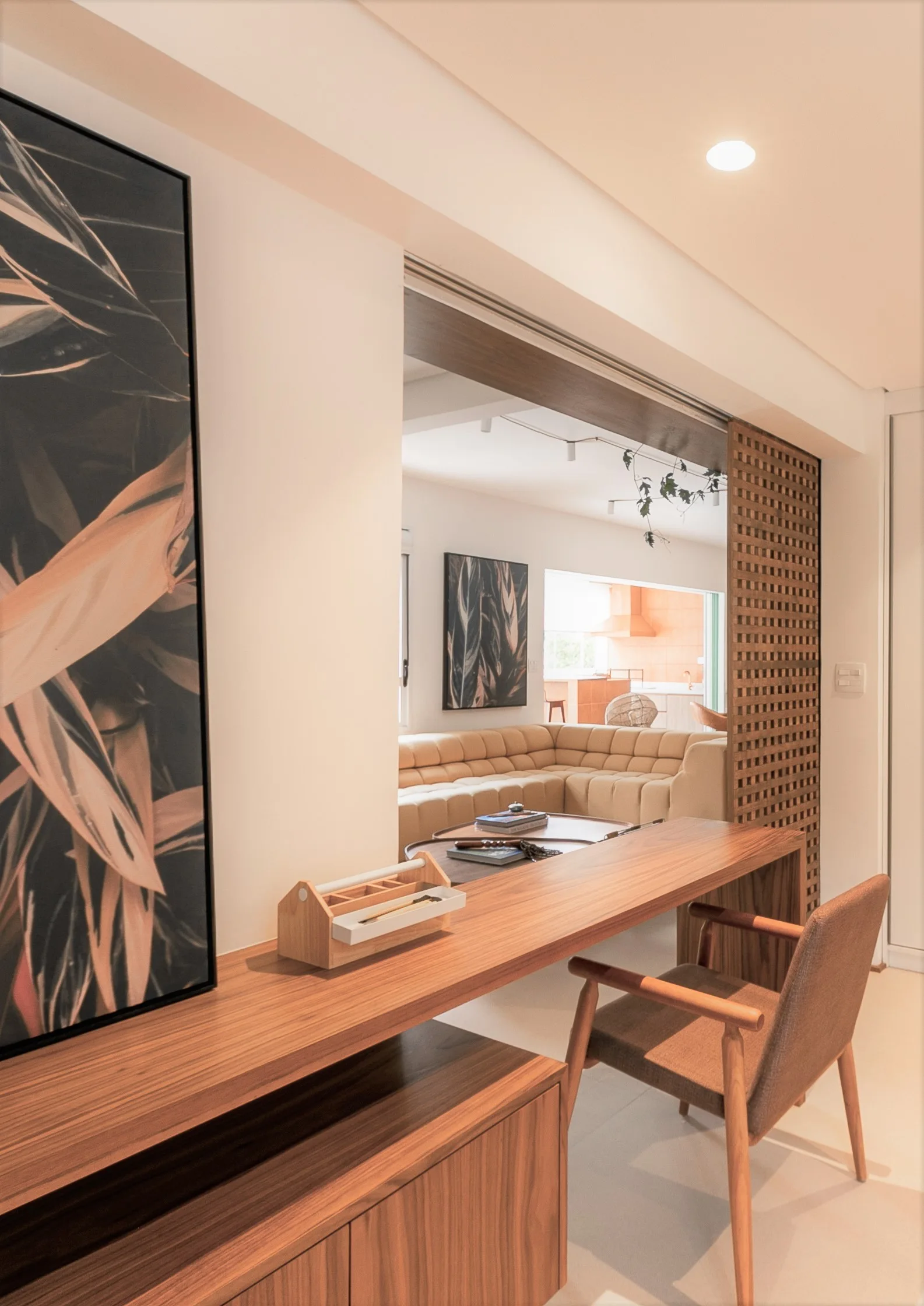 A wooden console desk with an armchair sits near a sliding partition showing a sectional sofa in the background.