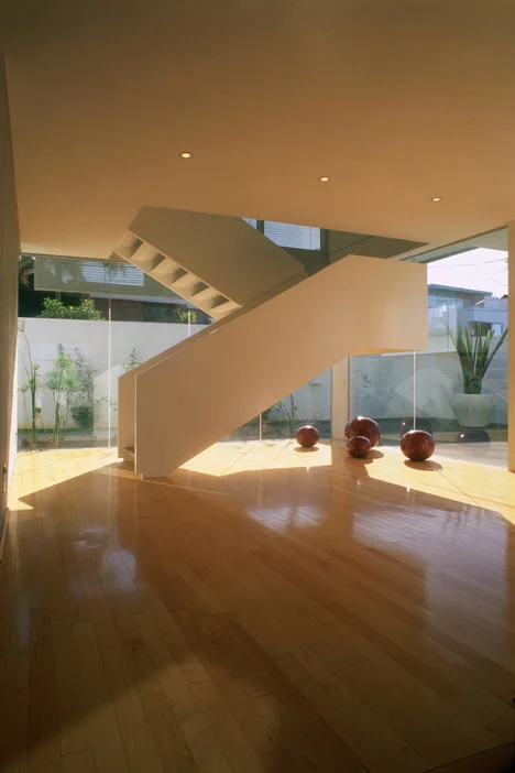 A minimalist off-white floating staircase sits on a polished hardwood floor in a room surrounded by floor-to-ceiling glass windows.