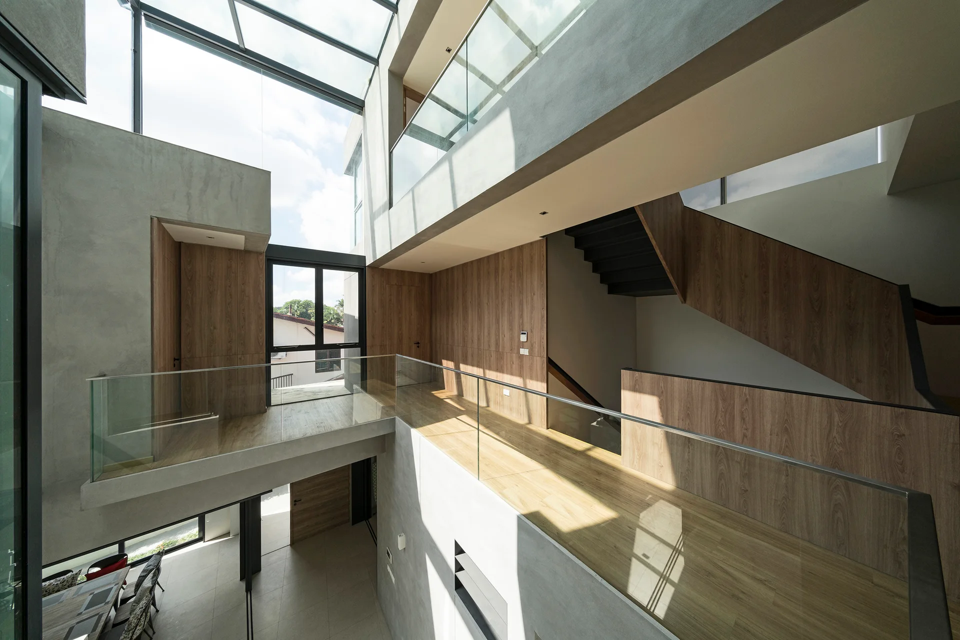 A modern multi-level landing features concrete-like walls, warm wood-toned paneling, clear glass railings, and a large overhead skylight.