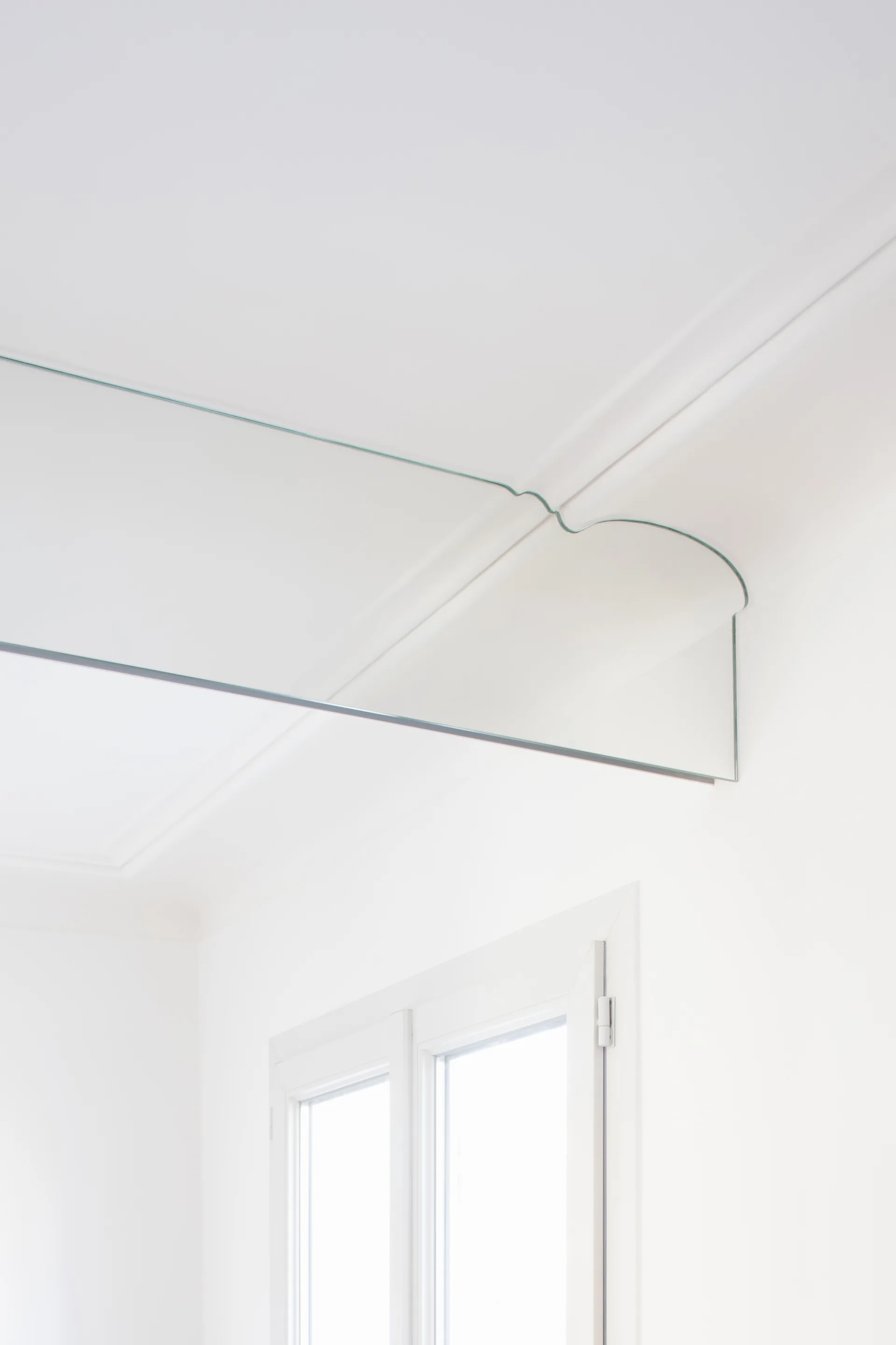 A custom-cut mirror panel is mounted on a white wall with its top edge shaped to precisely match the curves of the ceiling molding.