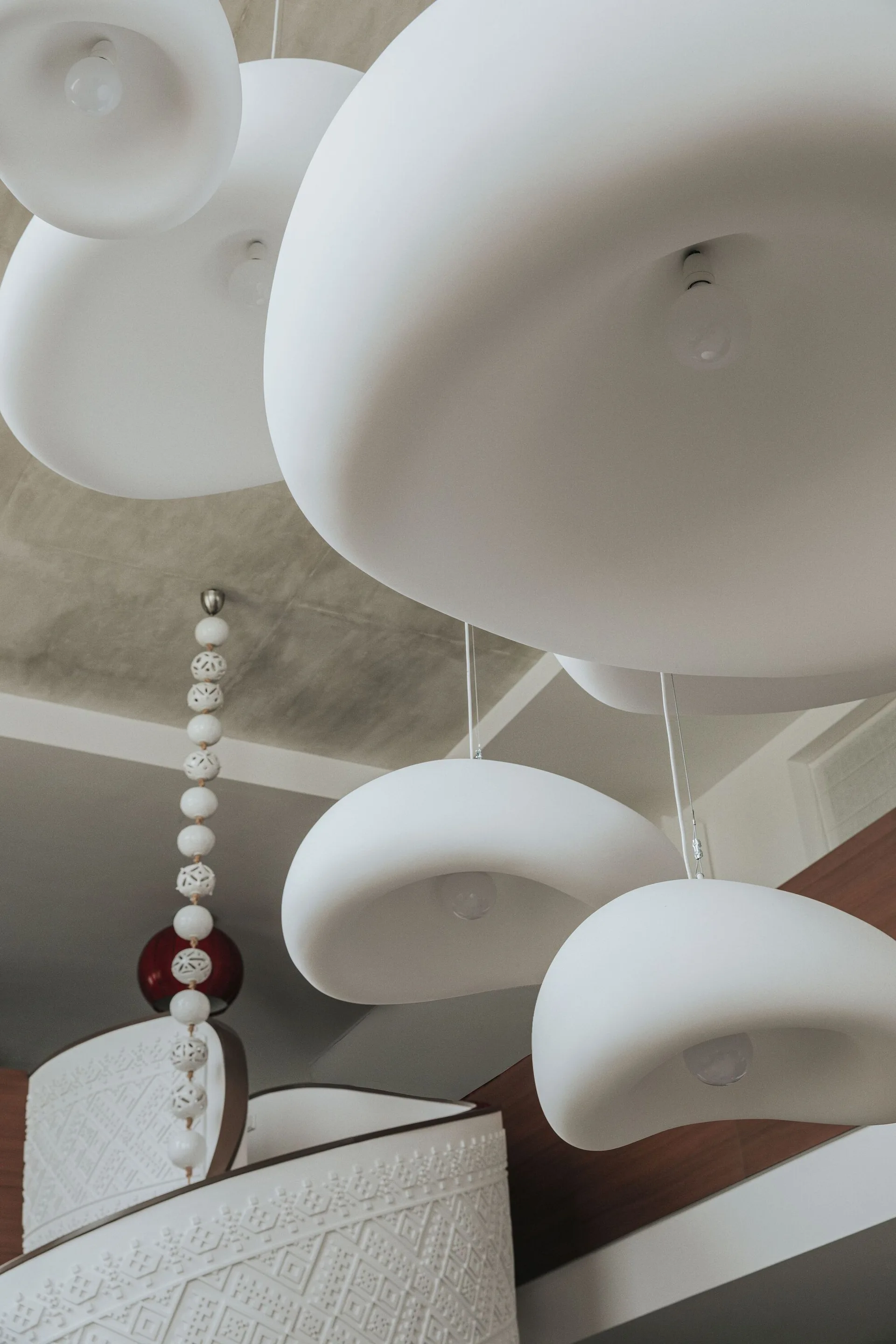 Matte white sculptural pendant lights hang from a textured ceiling near a curved white staircase decorated with carved geometric patterns.