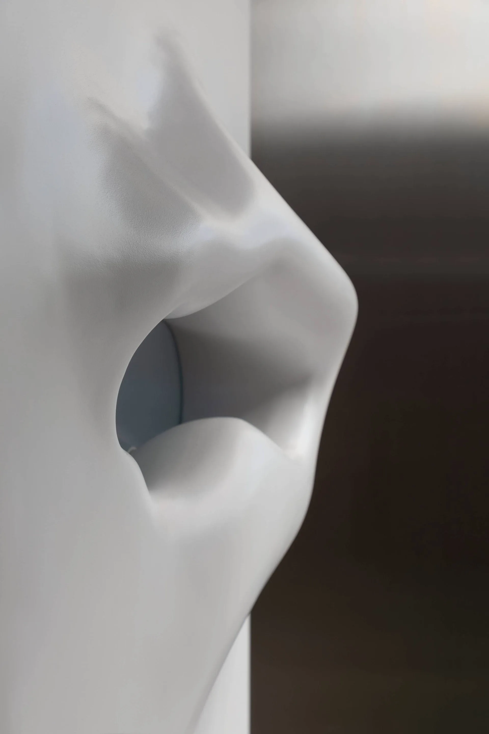 A close-up view of a smooth, white sculptural wall detail featuring an organic, lip-like contoured opening with a satin finish.