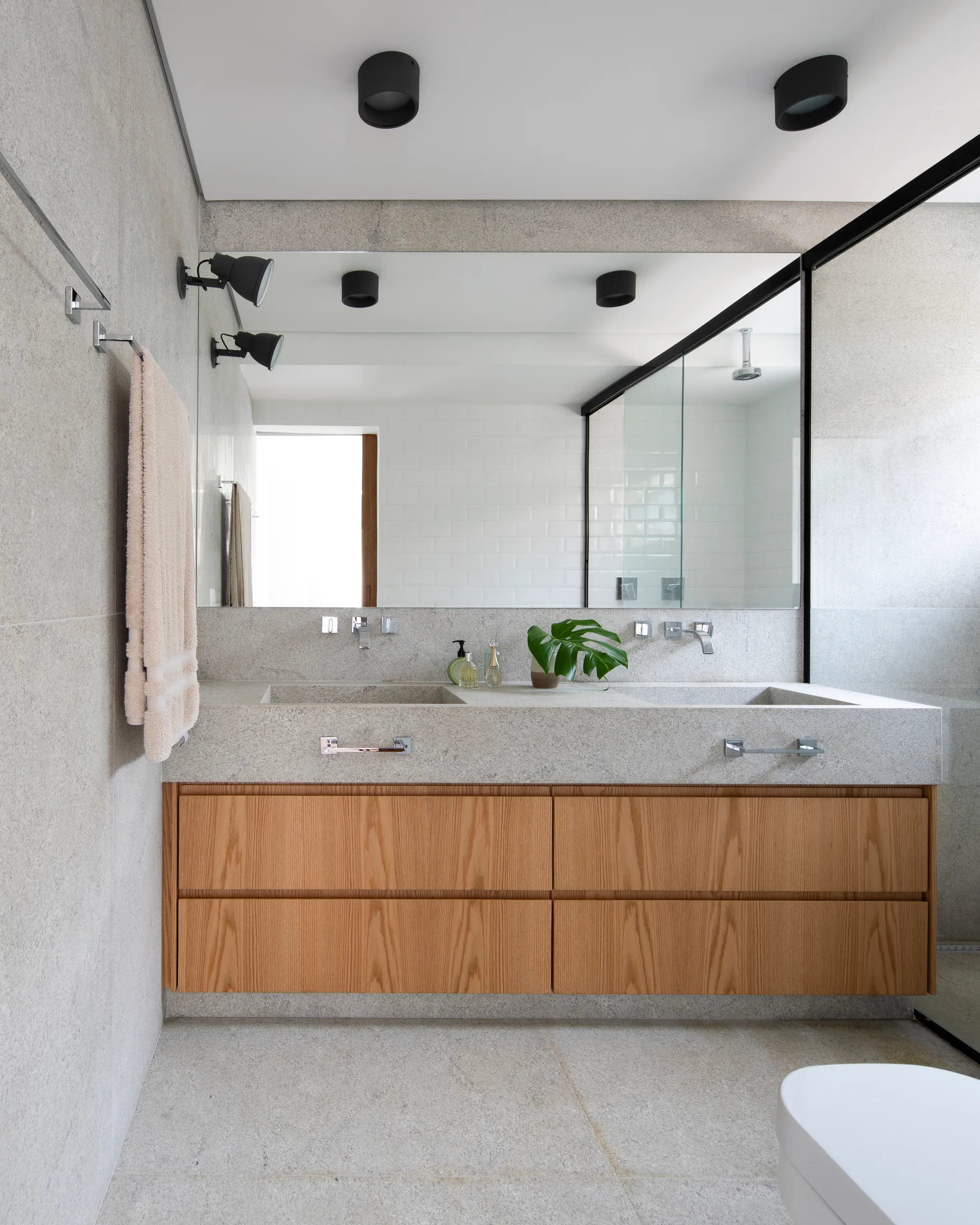 A modern bathroom features a stone double vanity with integrated basins, wood cabinetry, a large wall mirror, and grey stone tiled walls.