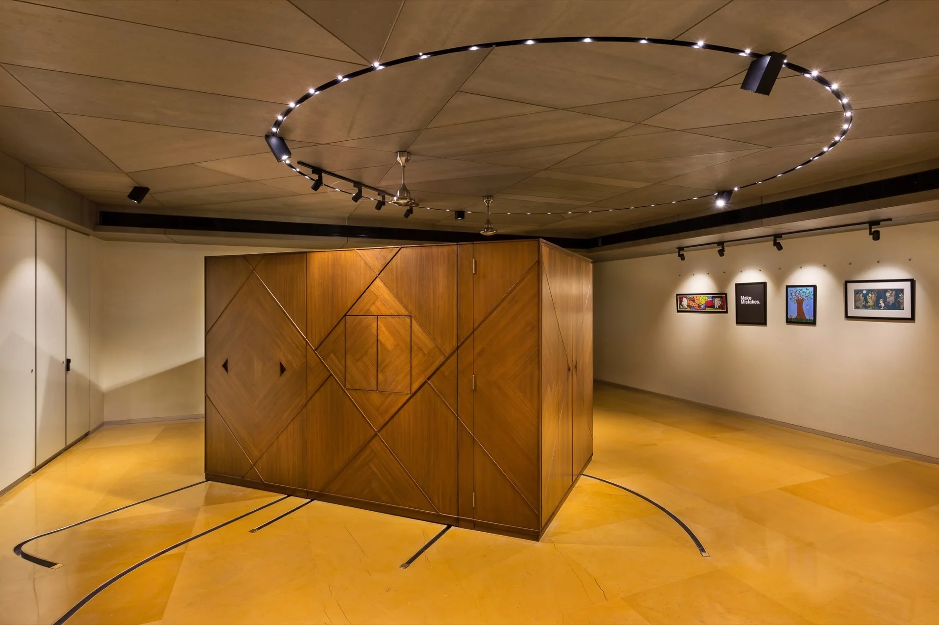 A large geometric wood cabinet stands on a polished yellow floor beneath circular ceiling track lighting in a minimalist gallery-style room.