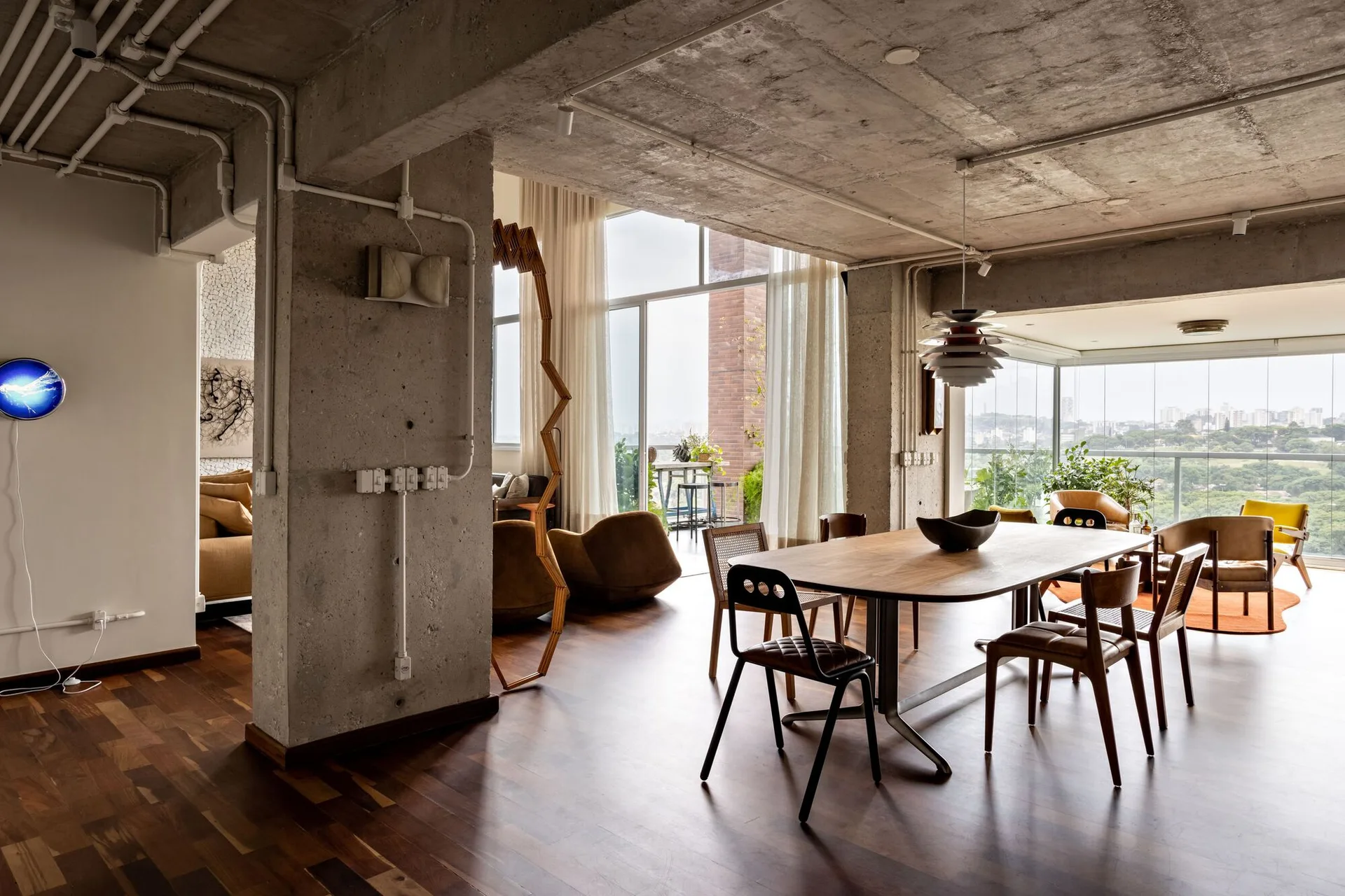 An open dining area with an oval wooden dining table, mismatched chairs, and a raw concrete ceiling and structural columns.