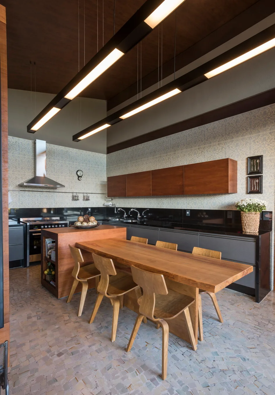 A modern kitchen with a long wooden dining table, matching bentwood chairs, dark gray lower cabinets, and linear pendant lights.