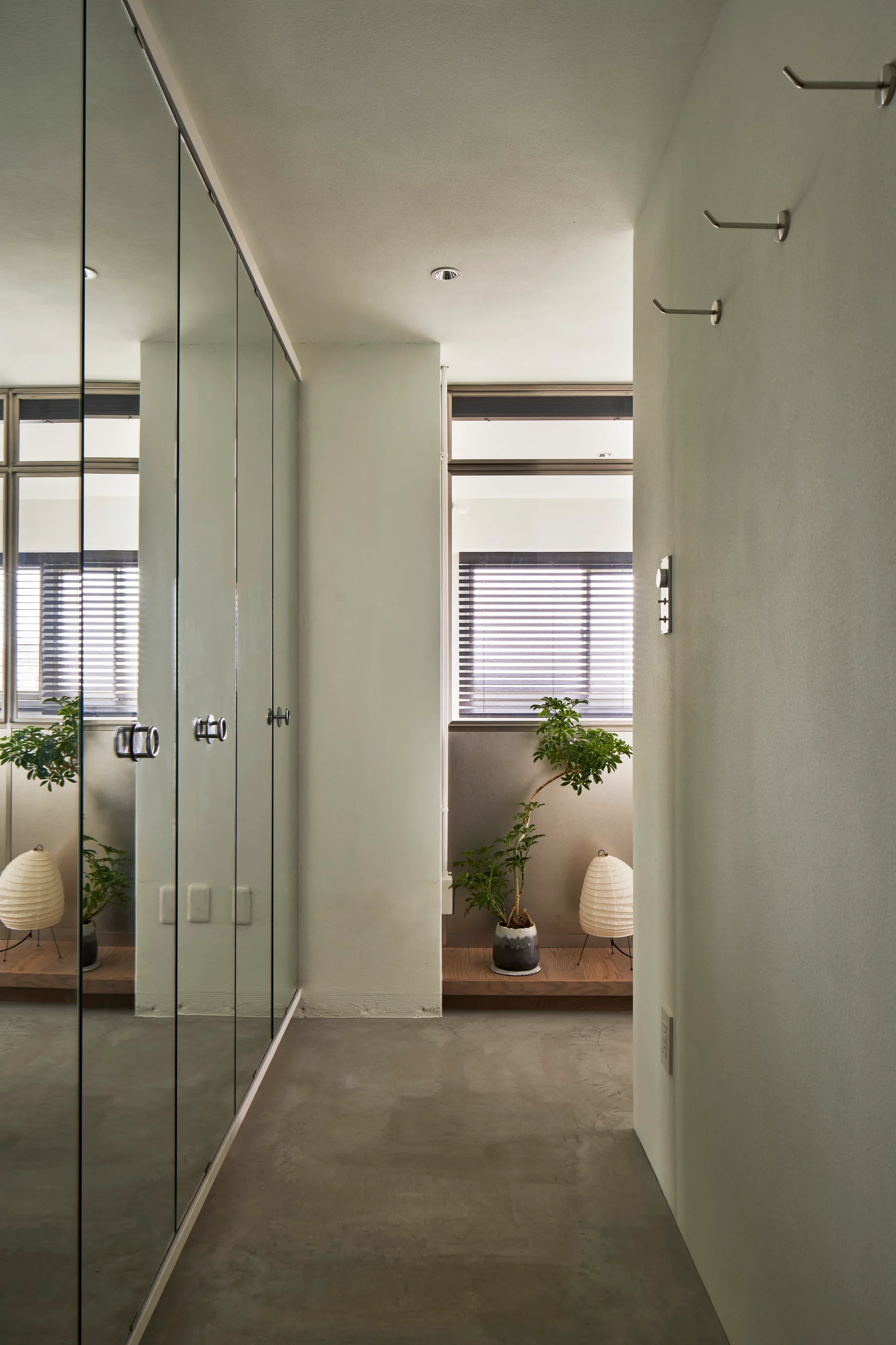 A minimalist hallway featuring floor-to-ceiling mirrored closet doors, a concrete floor, and a small potted tree near a paper lantern.