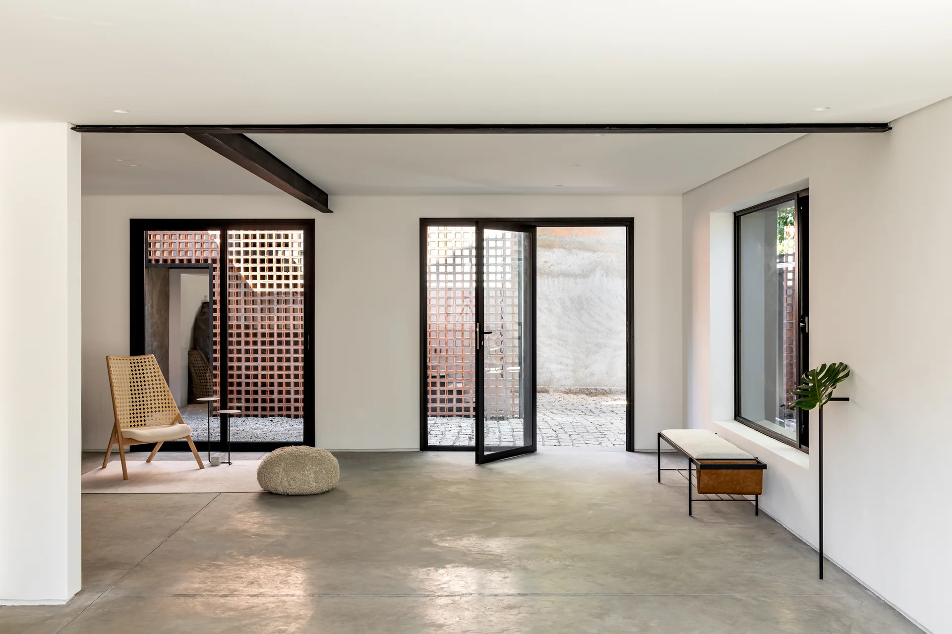 A minimalist living space with polished concrete floors, glass doors, and a decorative terracotta grid wall outside.