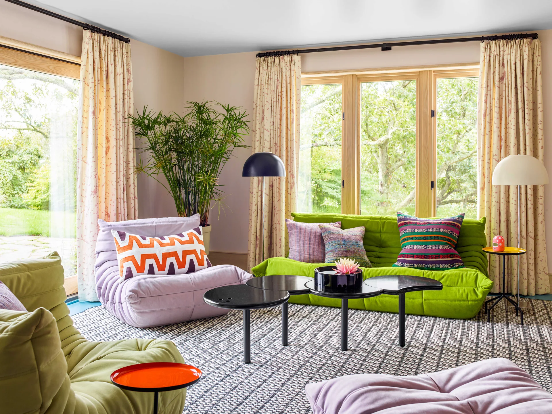 A bright living room features green and lavender tufted modular sofas arranged around a tiered black coffee table on a patterned rug.