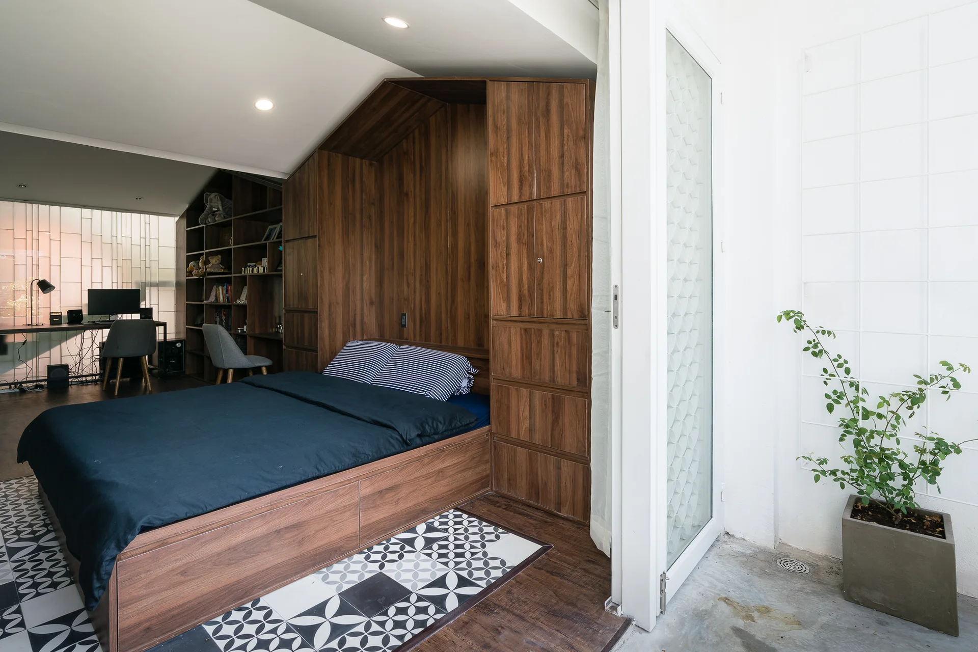A bedroom features a built-in wooden bed frame and storage unit next to a glass door opening onto a concrete patio.