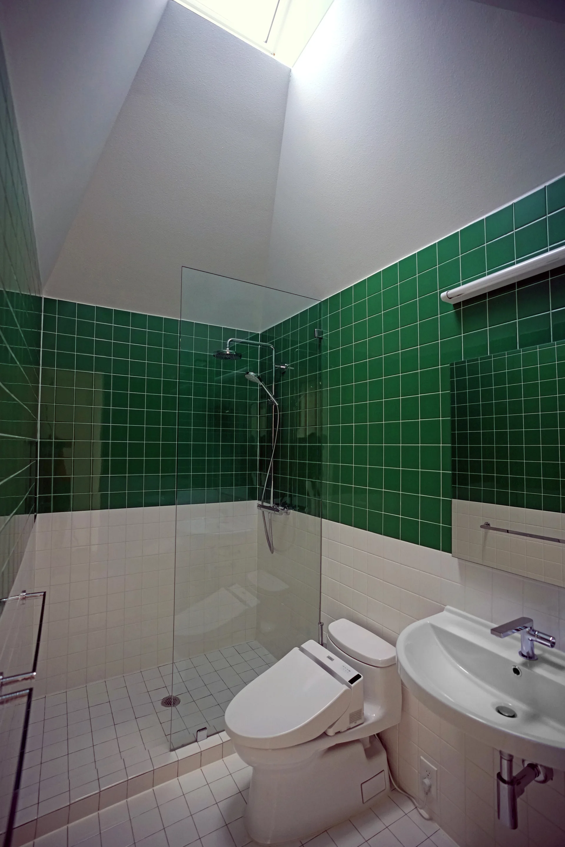 A modern bathroom featuring green and white tiled walls, a glass walk-in shower, a white bidet toilet, and a bright skylight.