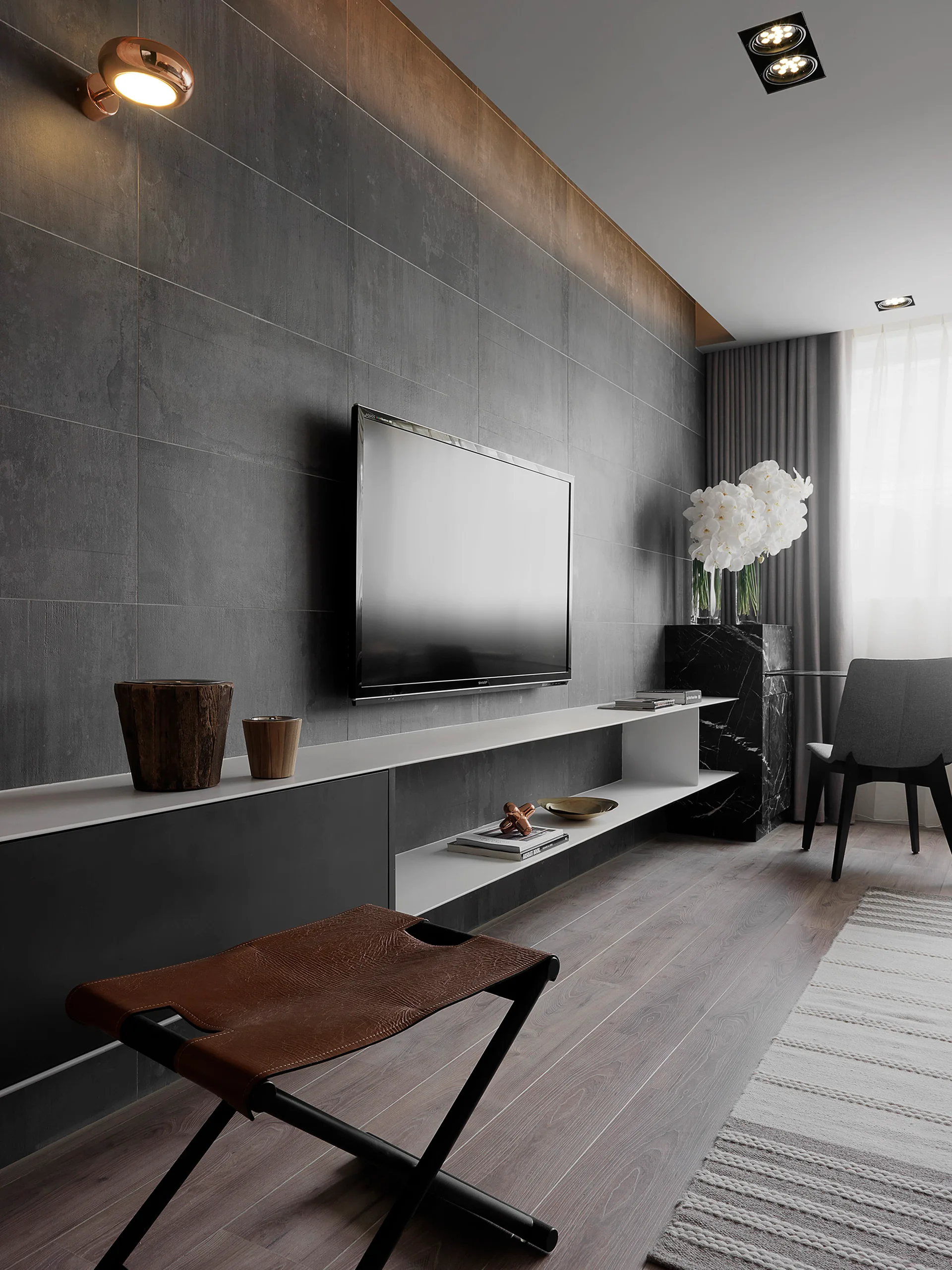 A modern living room featuring a dark grey tiled accent wall with a wall-mounted television and a long white floating console shelf.