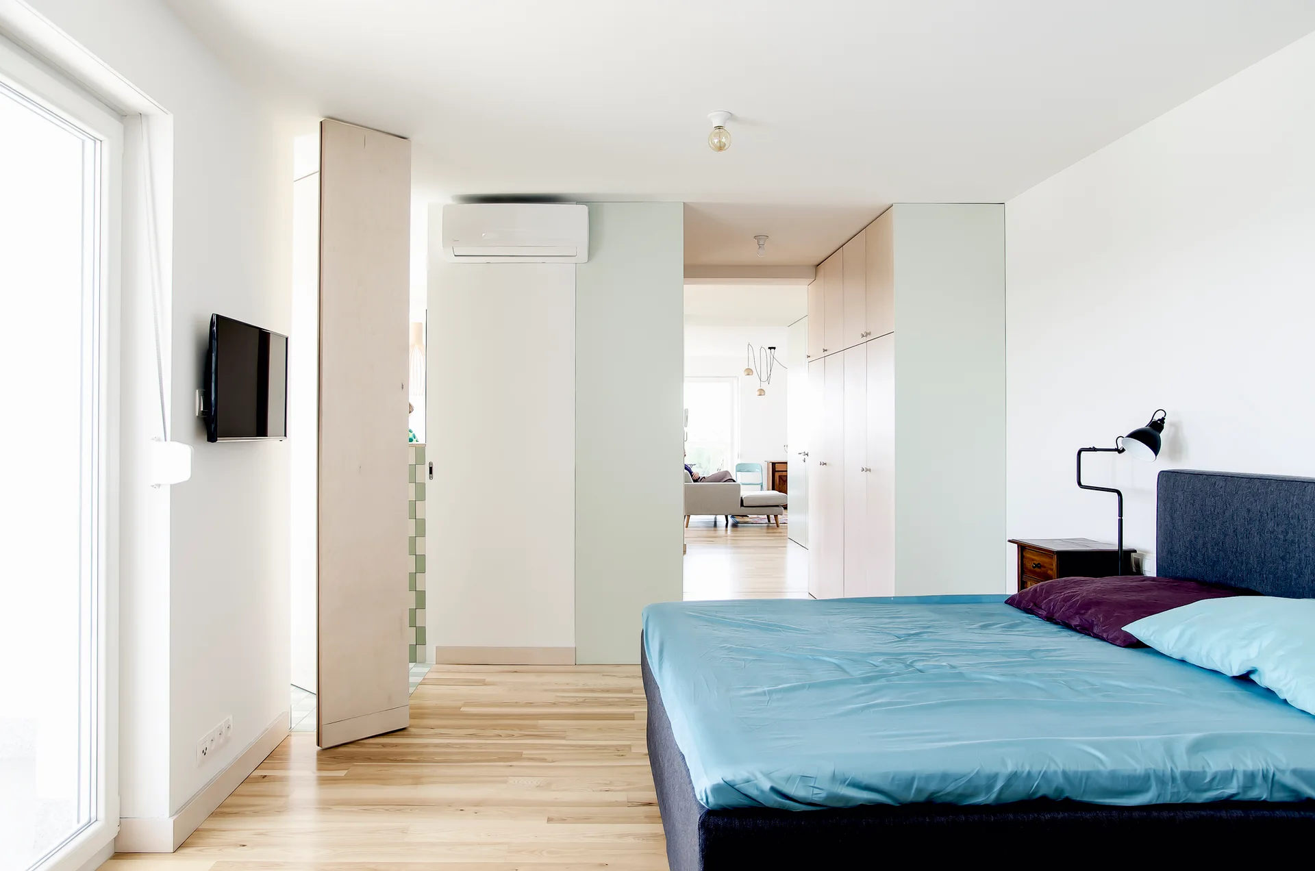 A modern bedroom featuring light wood flooring, a bed with blue bedding, and floor-to-ceiling built-in wooden closet cabinets.