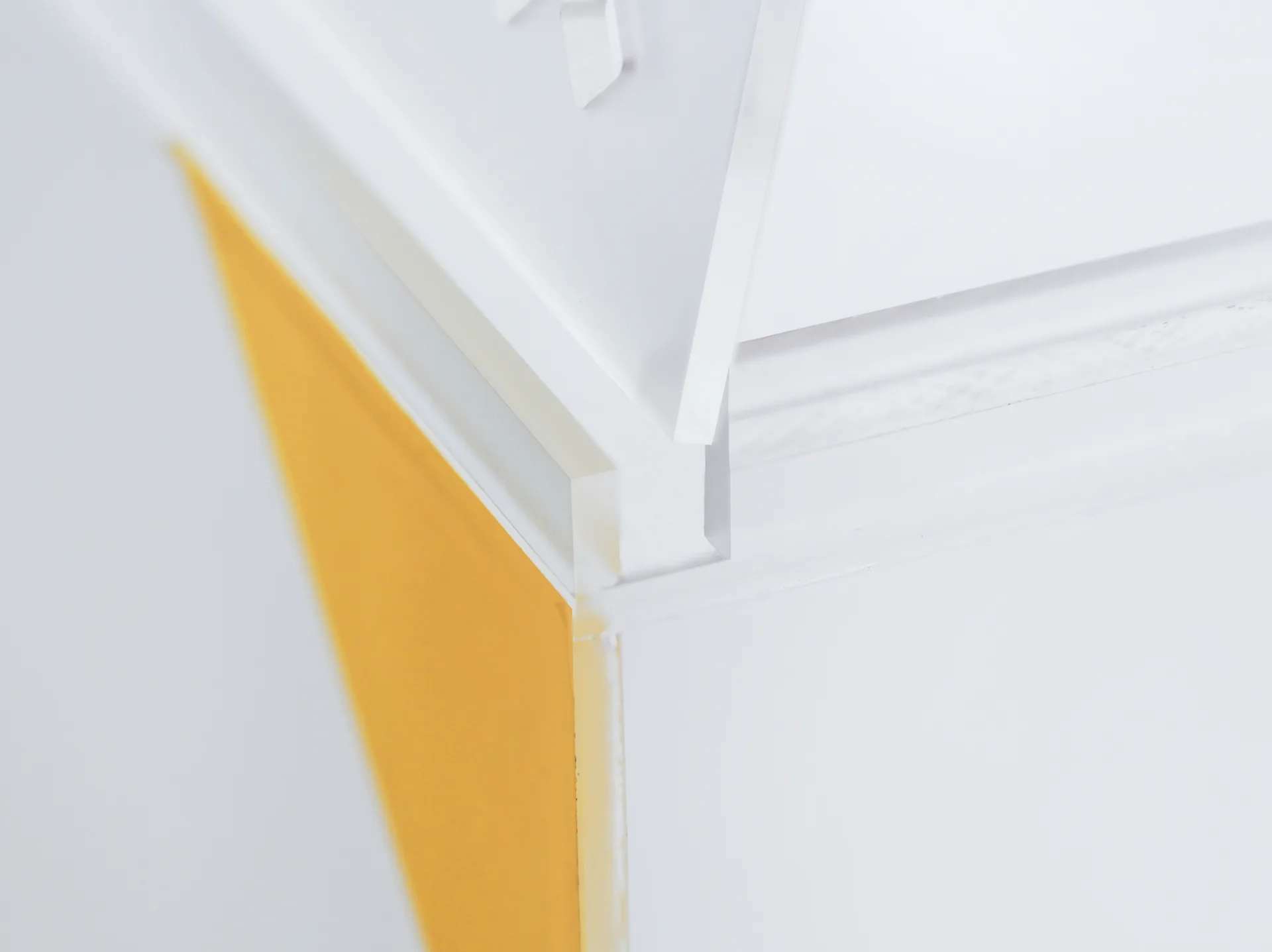 A close-up of a white geometric panel edge meeting a bright yellow accent strip at a precise mitered joint.