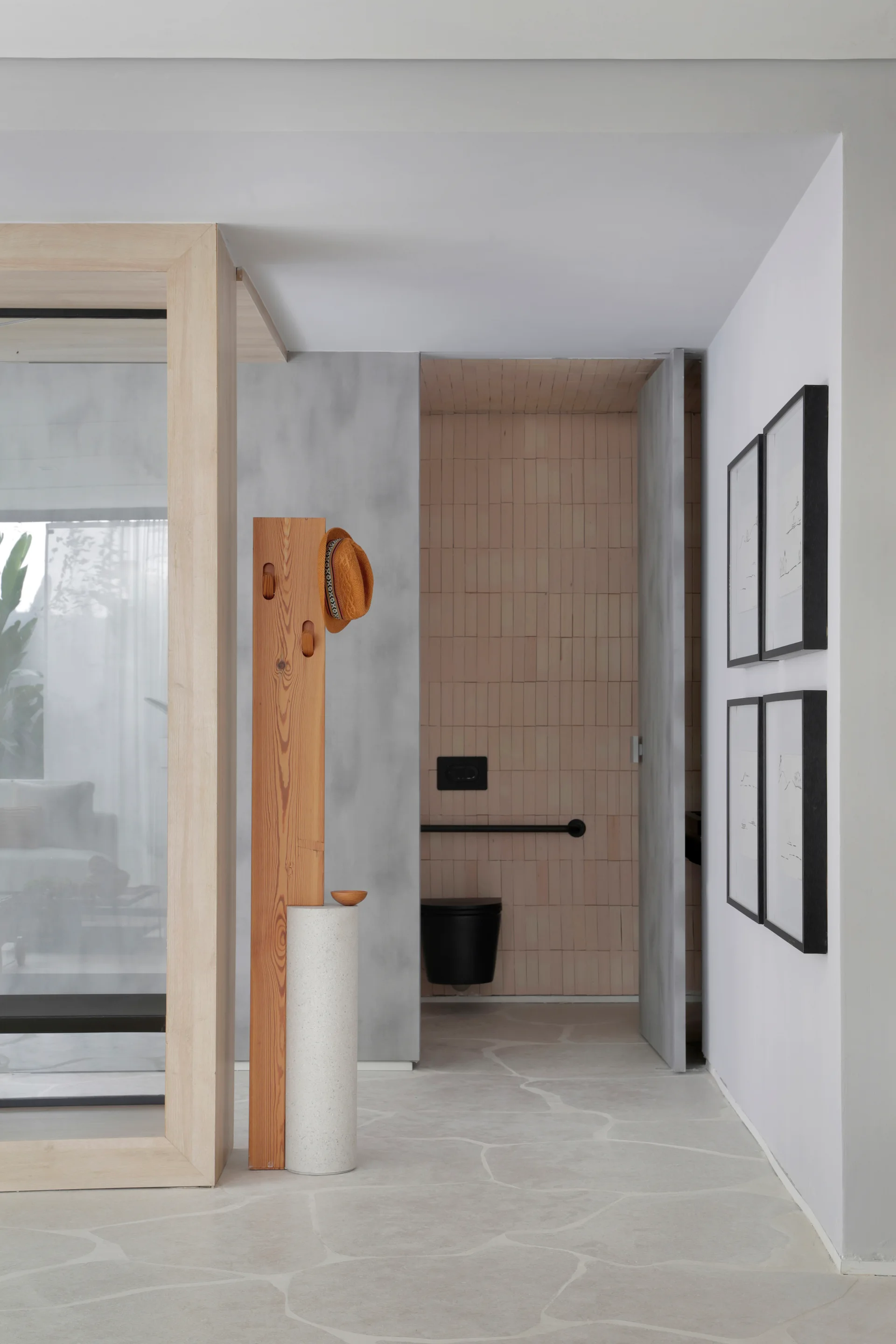 A modern hallway with a wood and stone coat rack leads to a bathroom with vertically stacked peach tiles and a black wall-mounted toilet.
