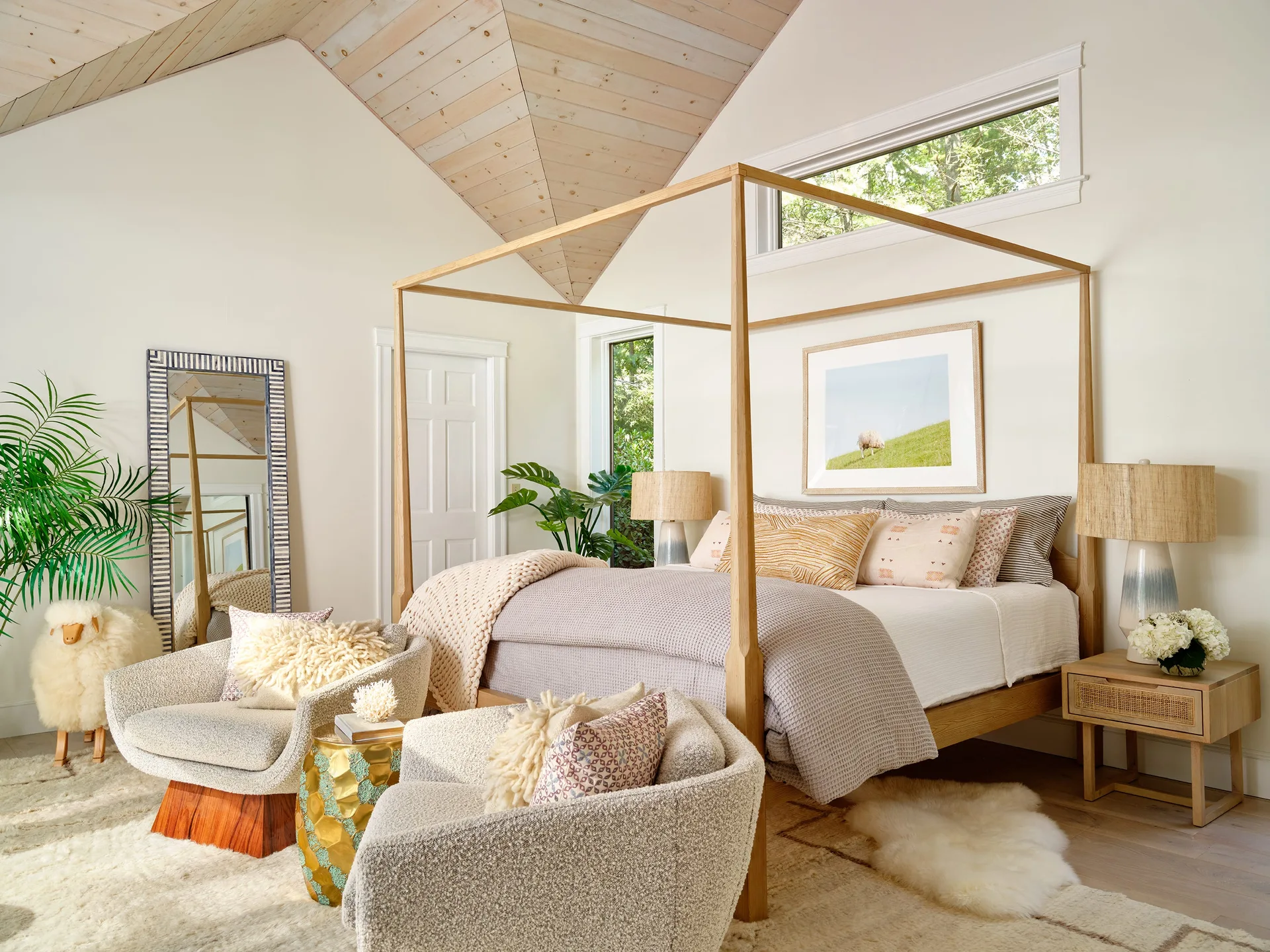 A light wood canopy bed sits under a vaulted wood-plank ceiling in a bedroom with textured armchairs and a soft shag rug.