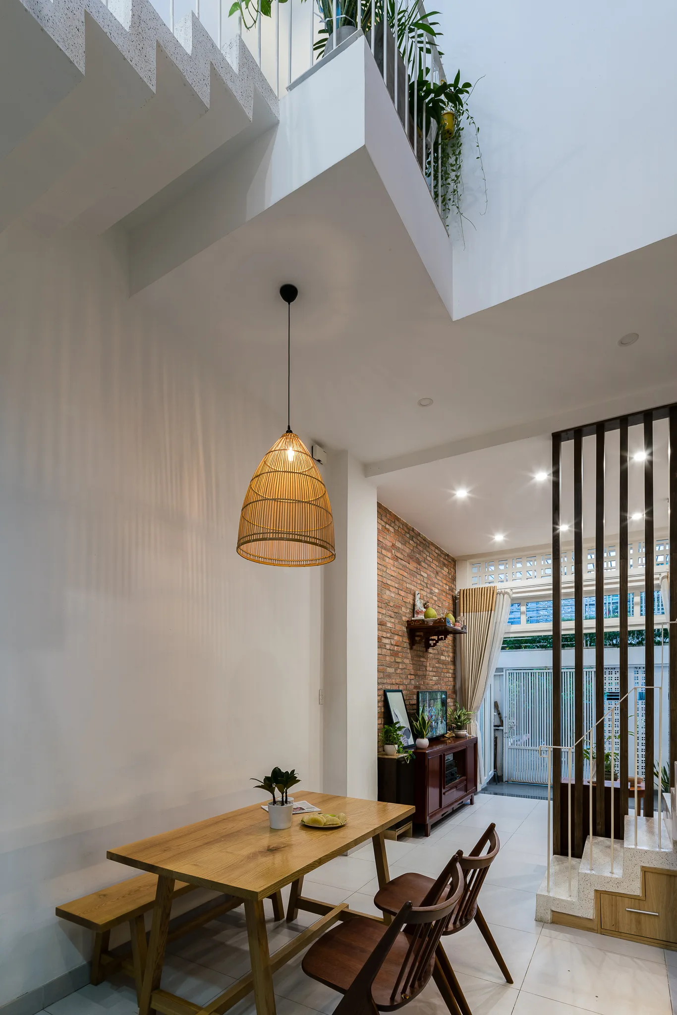 A modern dining area featuring a light wood table, a woven wicker pendant light, an exposed brick wall, and a vertical wood slat screen.