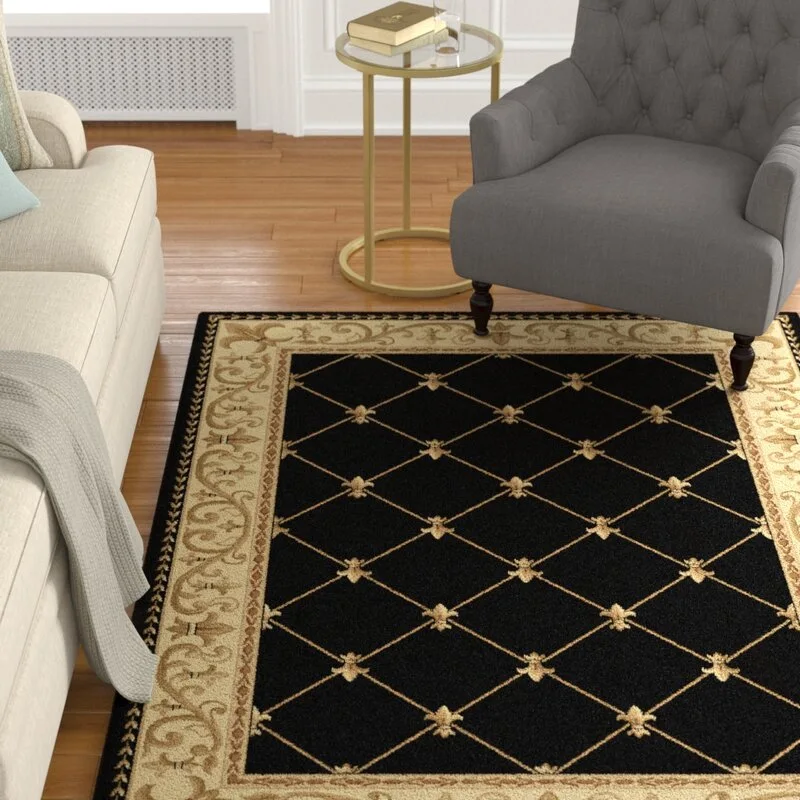 A black and gold diamond-patterned area rug lies on a wood floor between a cream sofa and a tufted grey armchair.