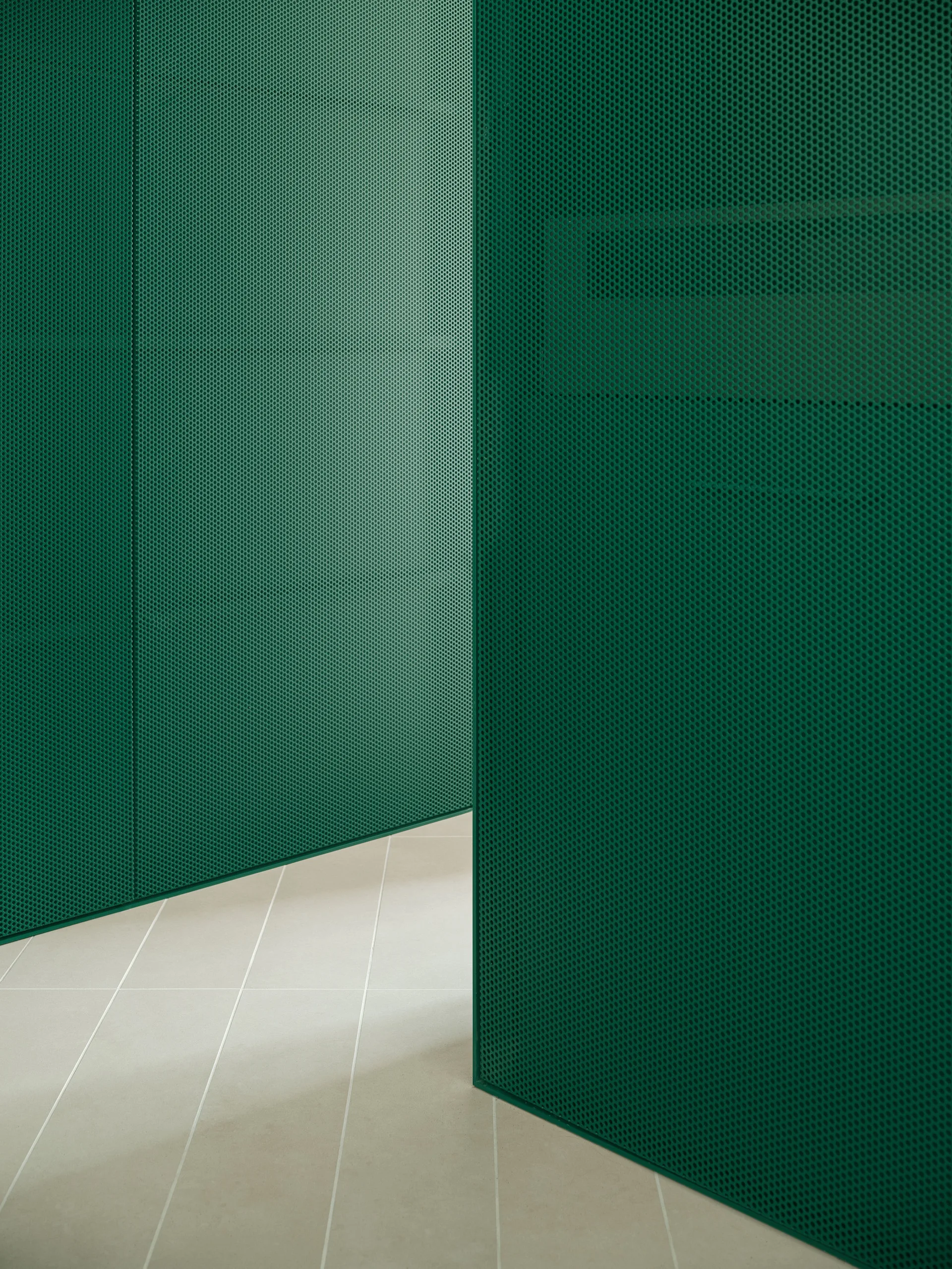 Matte emerald green perforated metal wall panels form a modern partition on a light off-white tiled floor.