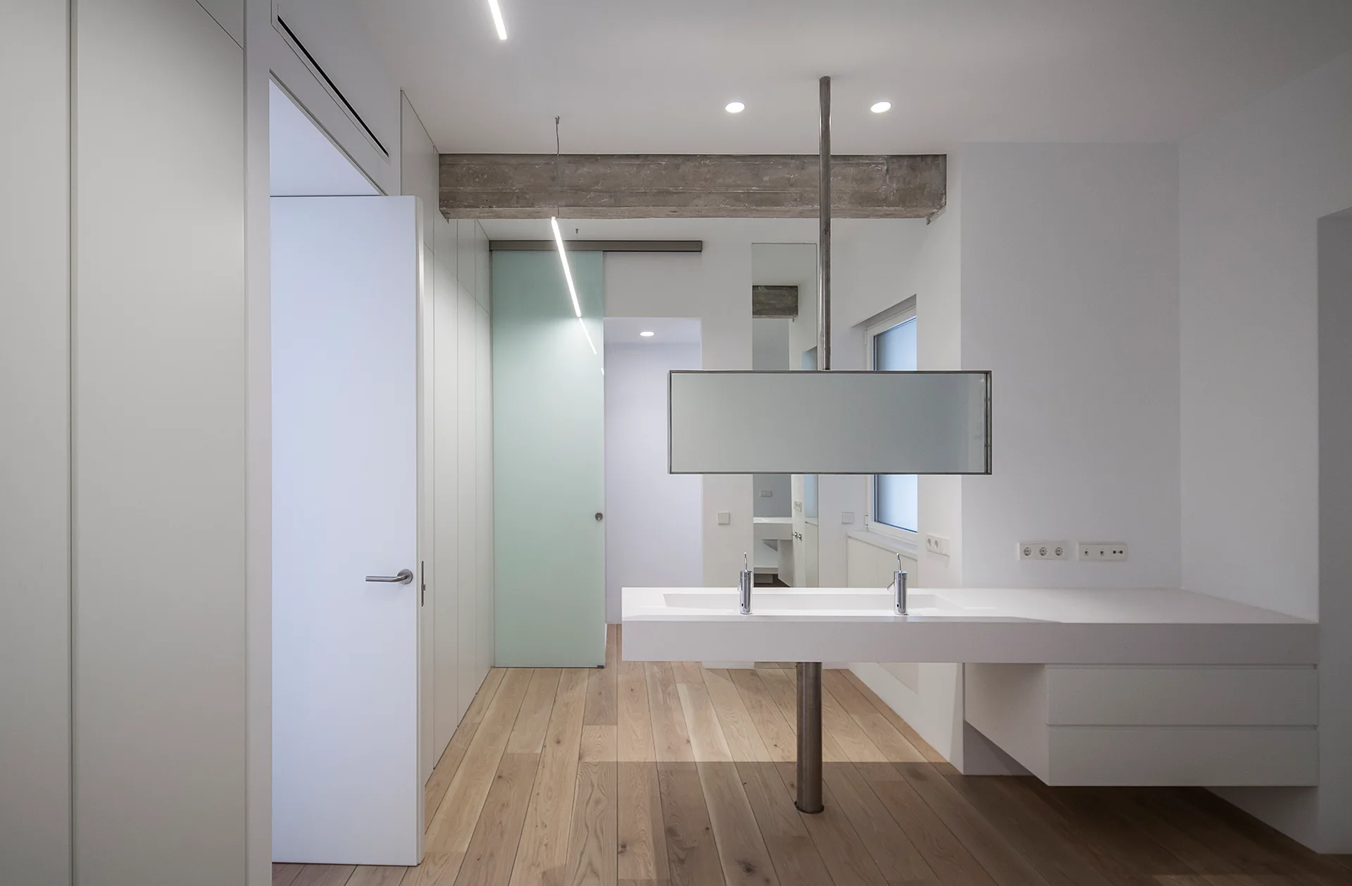 A minimalist bathroom features a floating white double vanity with a ceiling-hung mirror, light wood floors, and a pale green sliding glass door.