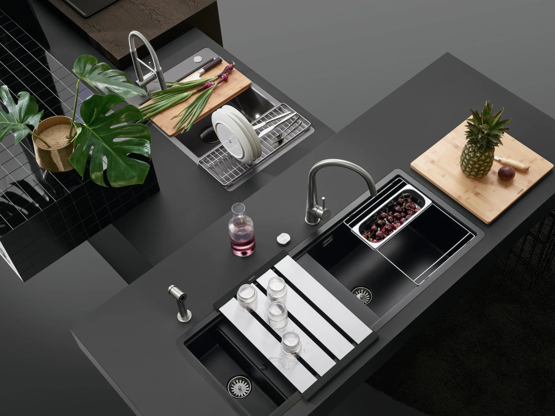 A high-angle view of a matte black kitchen countertop featuring two integrated sinks with silver faucets, wooden cutting boards, and metal drying racks.