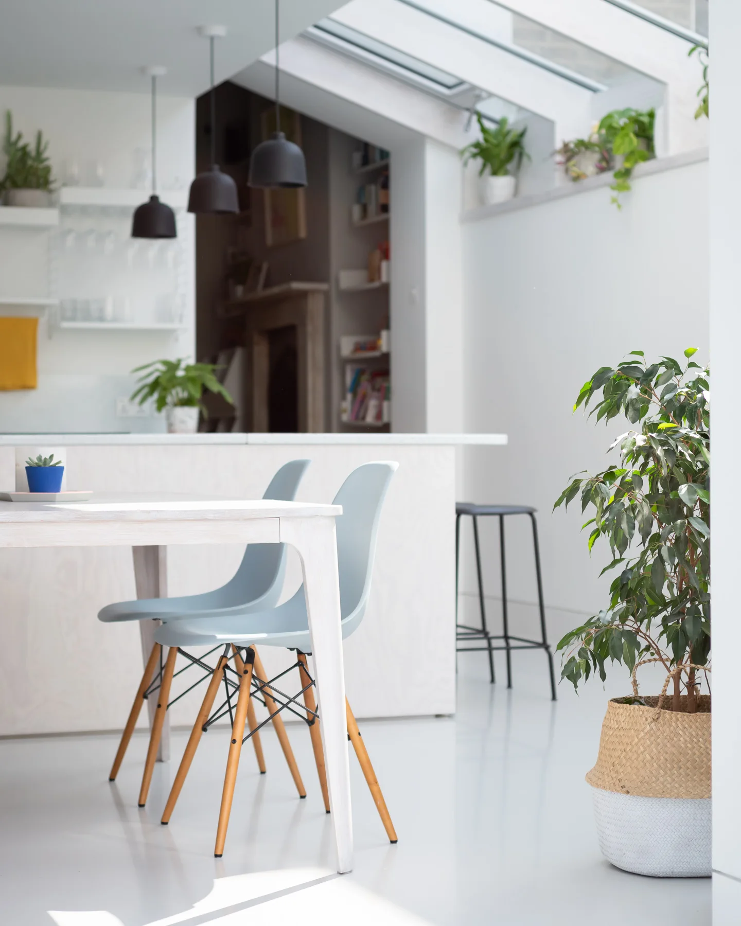 A bright dining room features a white wooden table with grey molded chairs beneath a slanted skylight ceiling and hanging black pendant lights.