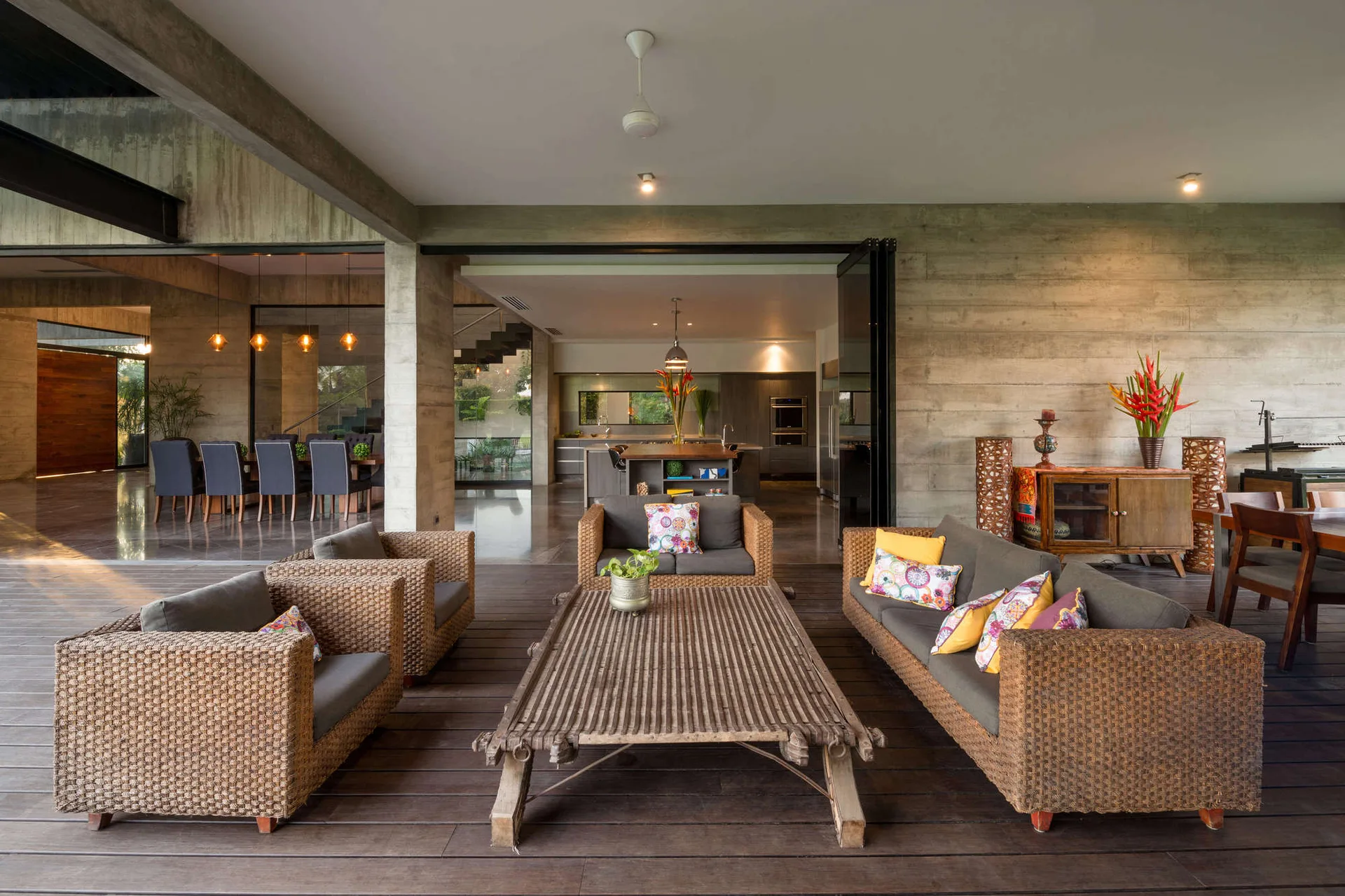 A covered outdoor patio featuring woven wicker sofas and matching armchairs arranged around a rustic wood coffee table on a dark wood deck.