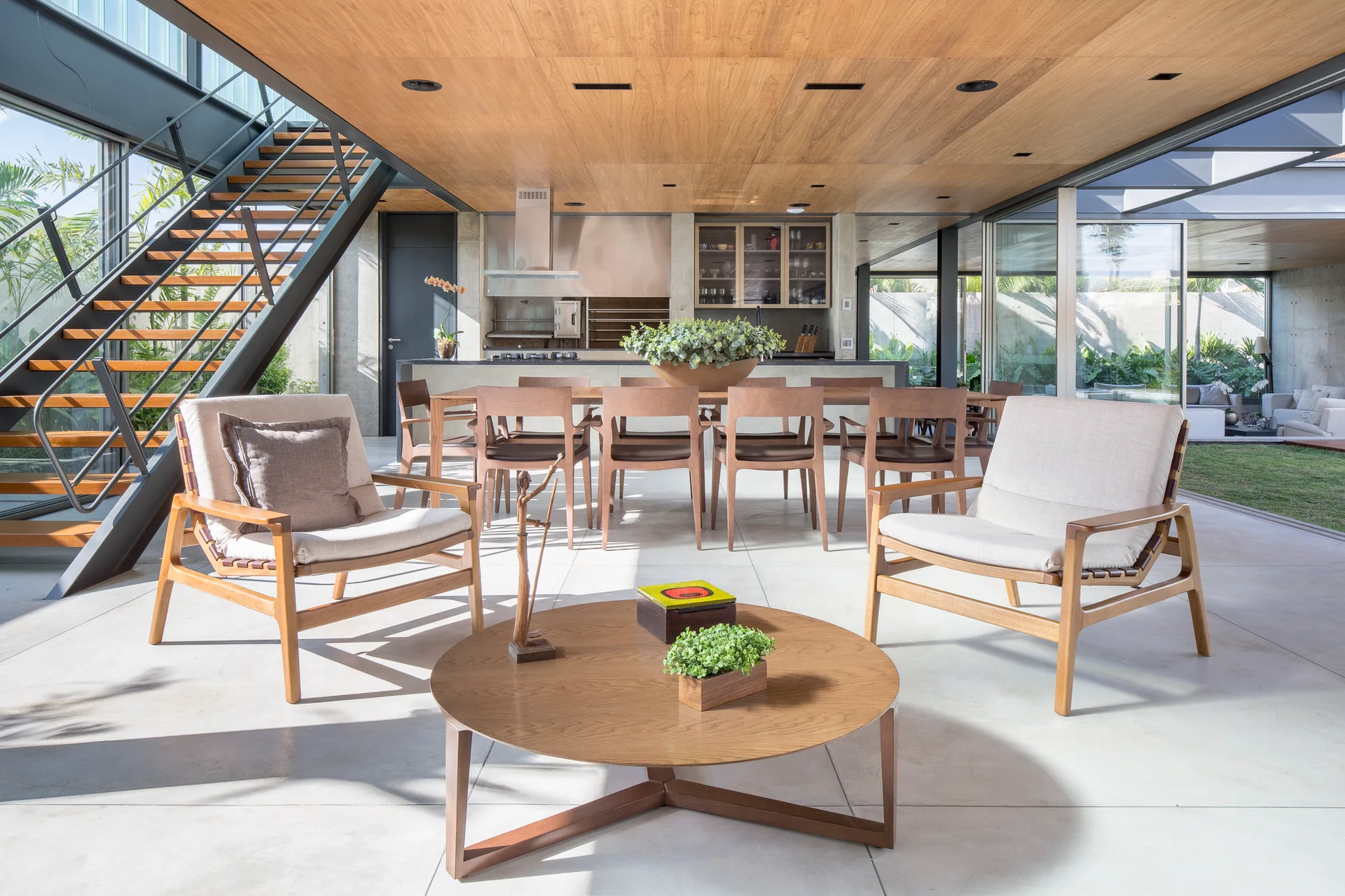 A modern open-concept living area with a wood ceiling, two beige armchairs, a round coffee table, and an open metal staircase.