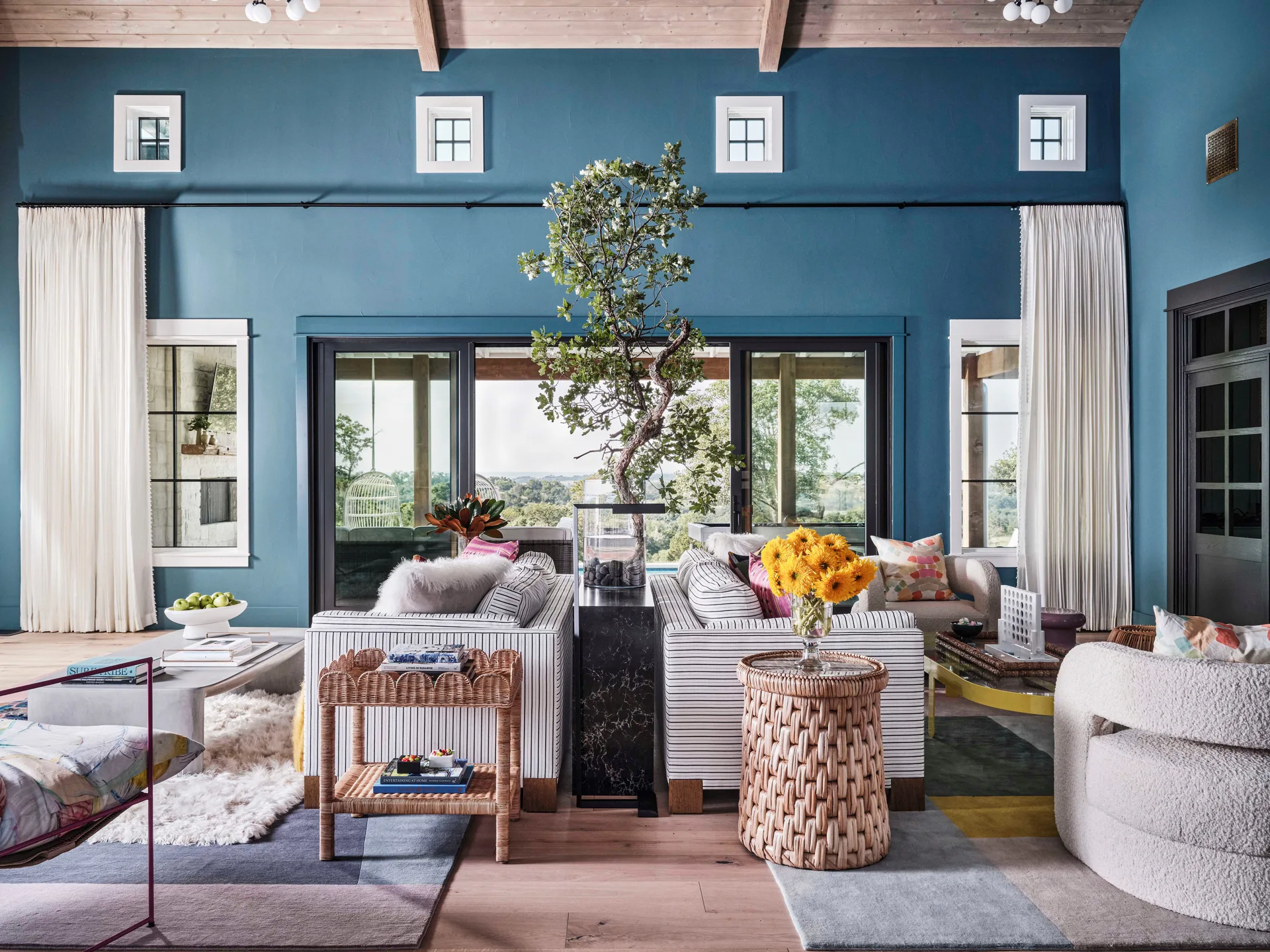 A spacious living room features teal walls, a light wood plank ceiling, two back-to-back pinstriped sofas, and sliding glass doors.