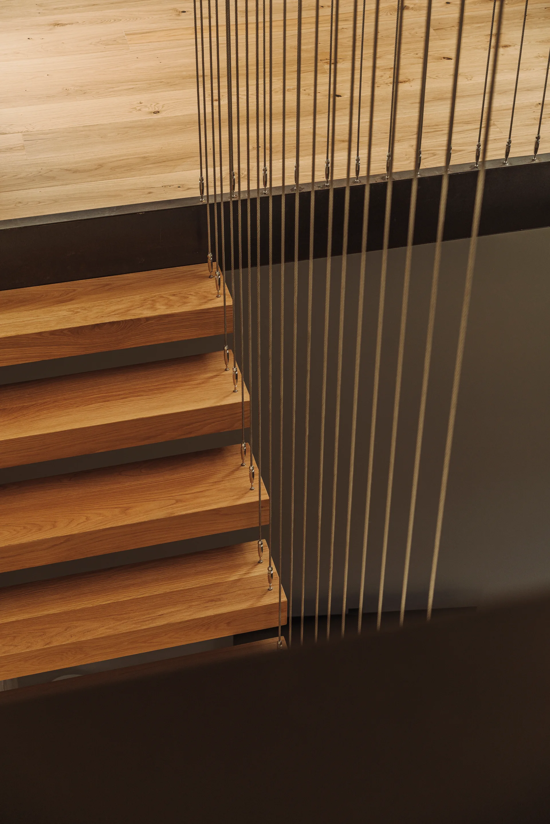 A modern staircase featuring thick wood treads, a matching upper floor, and a minimalist balustrade of vertical metal cables.