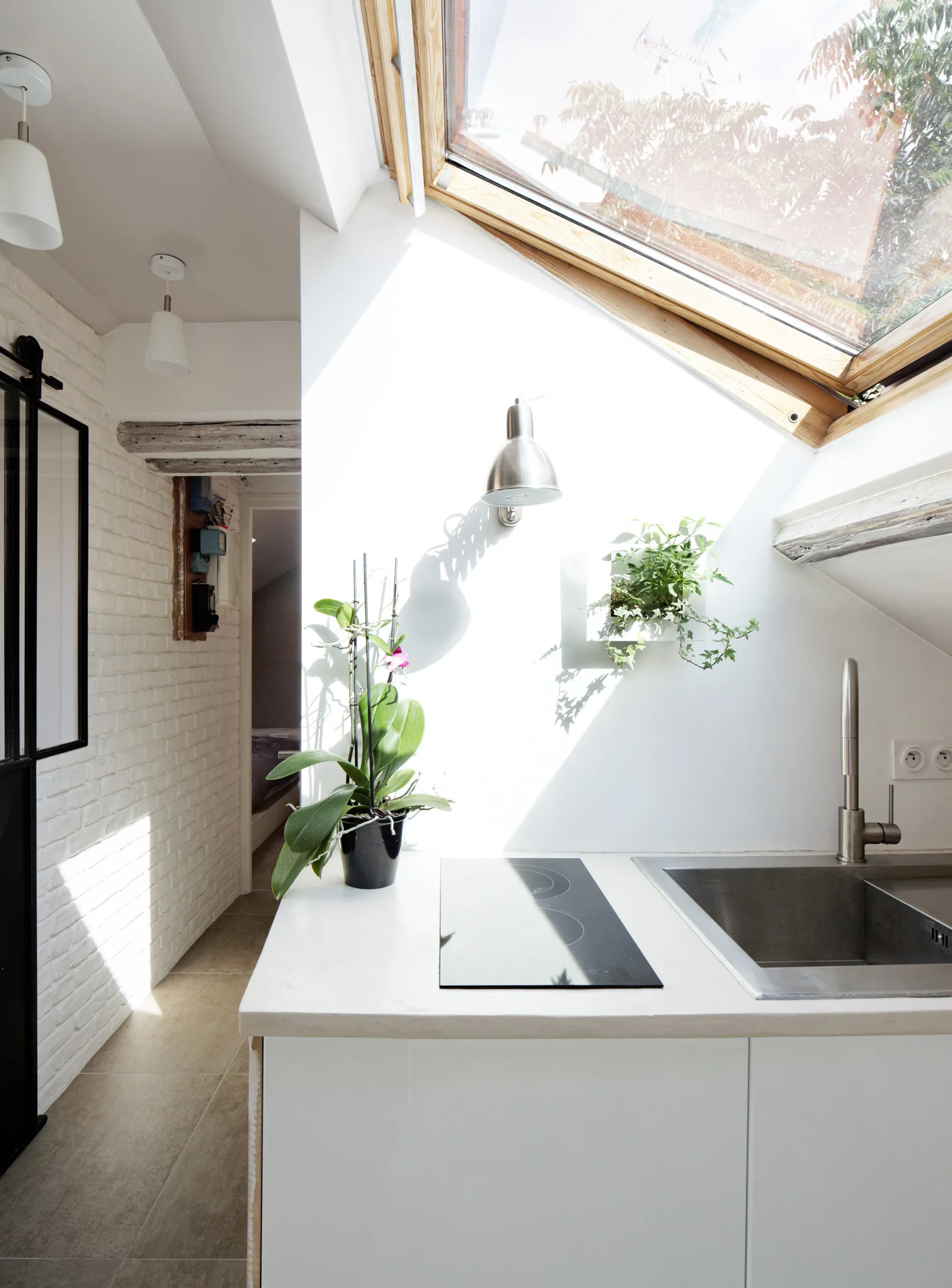 A compact attic kitchen with white cabinetry, a stainless steel sink, and a large sloped skylight overhead.