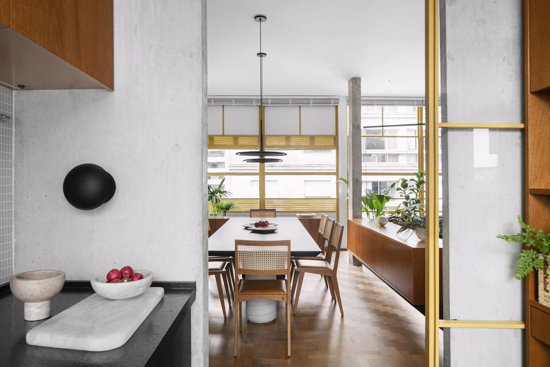 A modern dining room featuring a dark table with wood and cane chairs, parquet flooring, and large yellow-framed windows.