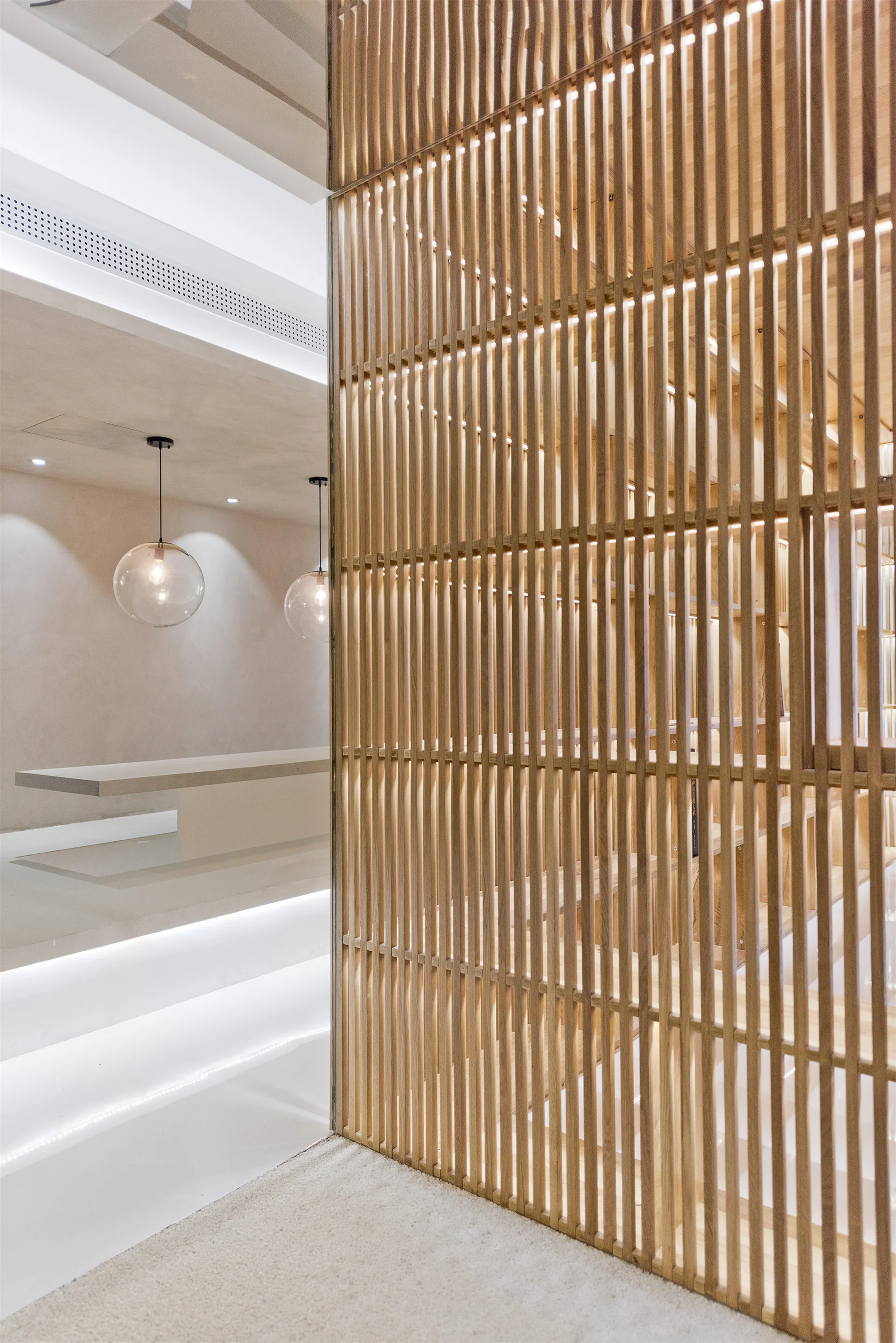 A minimalist interior featuring a tall slatted wood divider next to concrete-look steps lit by under-tread LED strip lights.