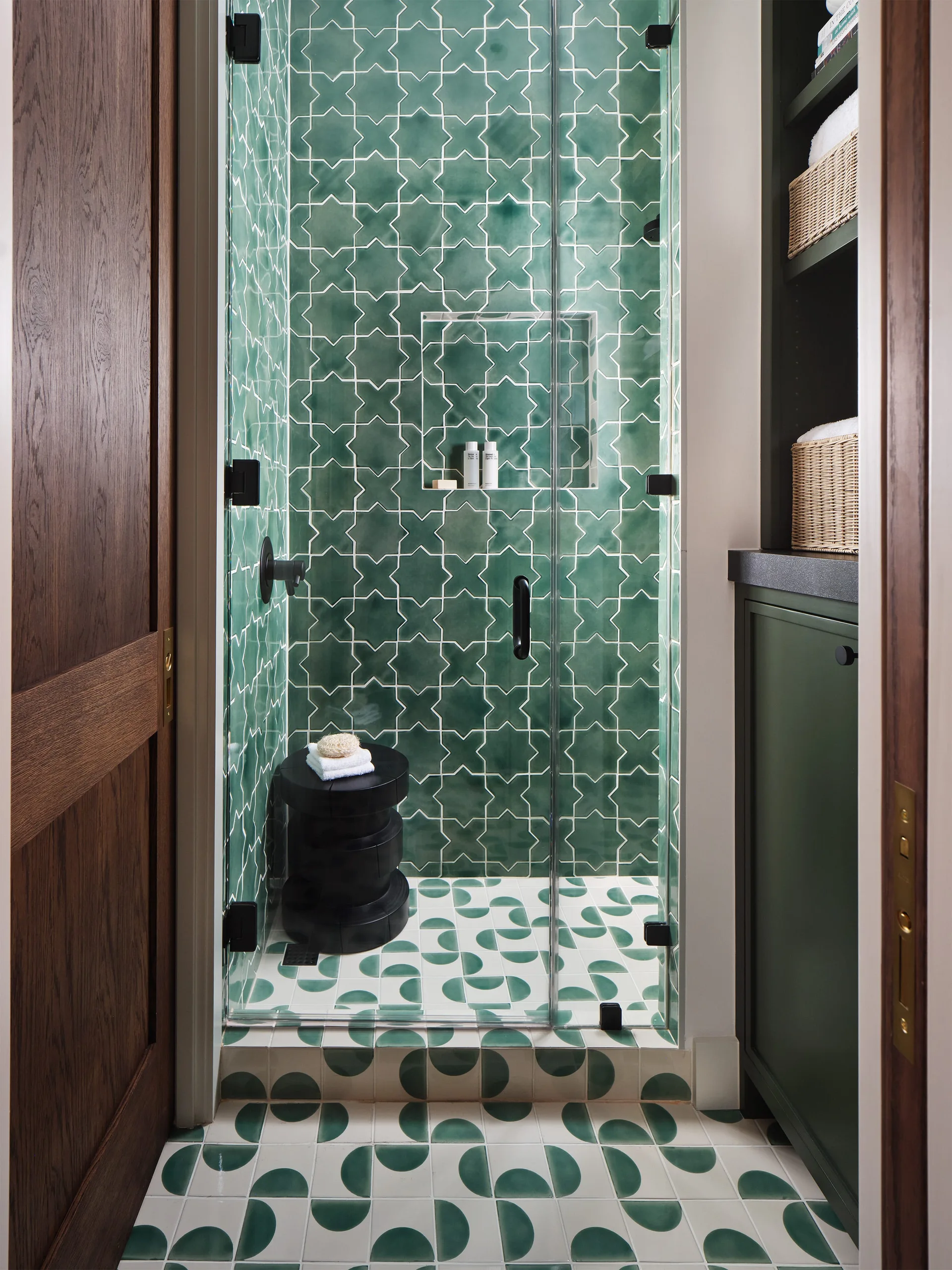 A glass-enclosed walk-in shower features green star-patterned wall tiles, semi-circle patterned floor tiles, and an adjacent dark green built-in cabinet.