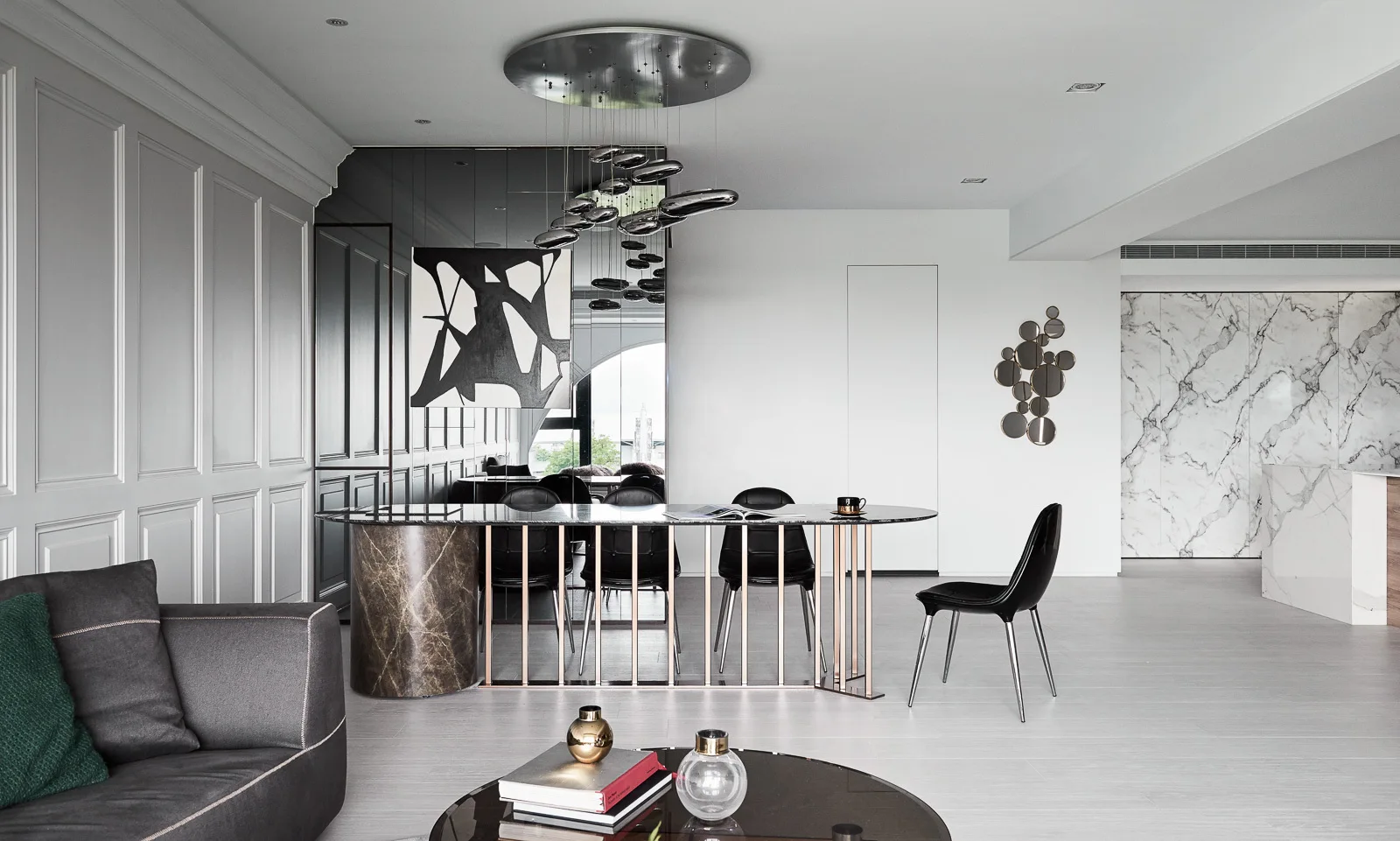 A contemporary open-plan dining area features a black marble pedestal table, dark leather chairs, a mirrored accent wall, and metallic pendant lights.