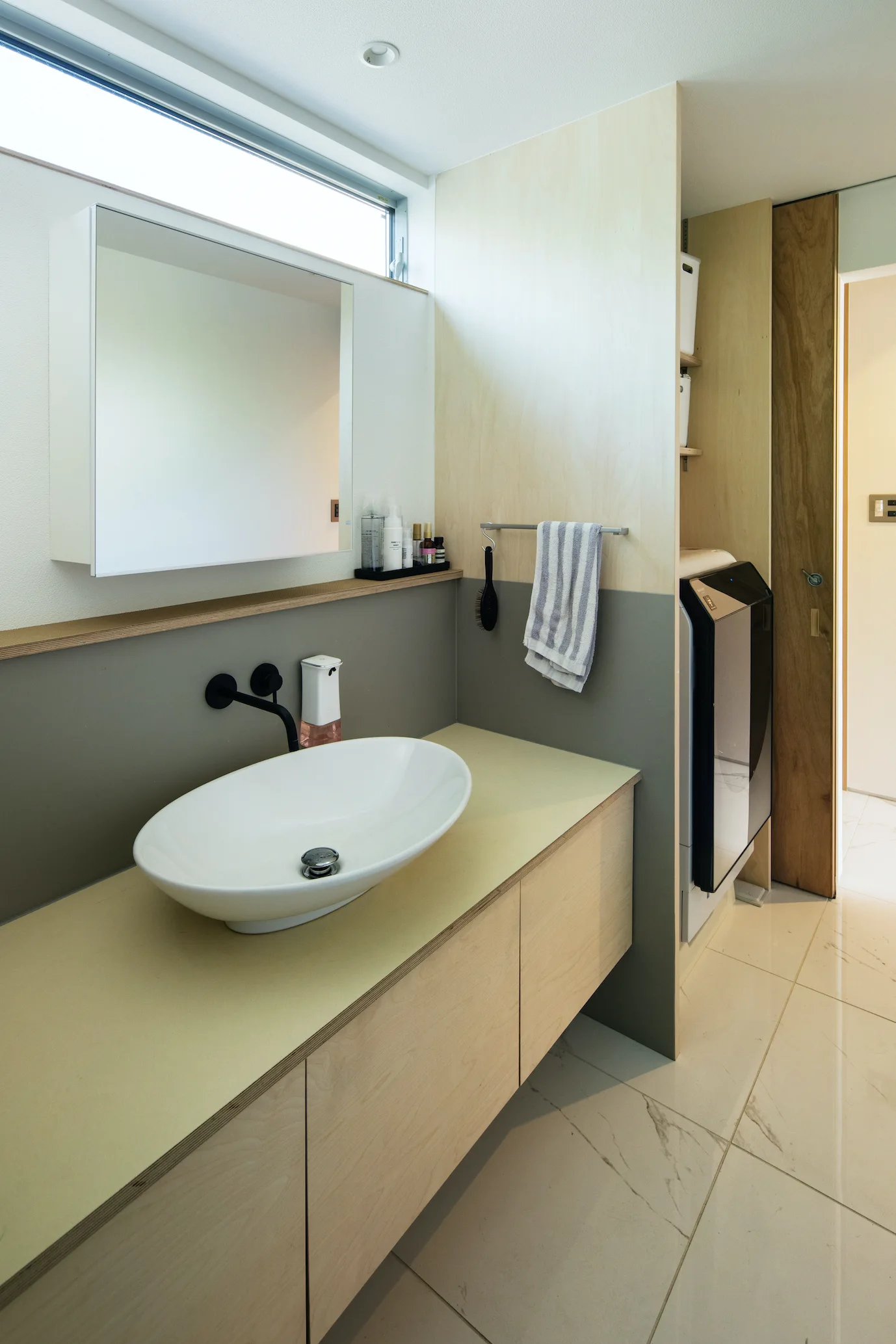 A modern bathroom features a light wood vanity with an oval vessel sink, a matte black wall-mounted faucet, and a dual-tone grey and wood accent wall.