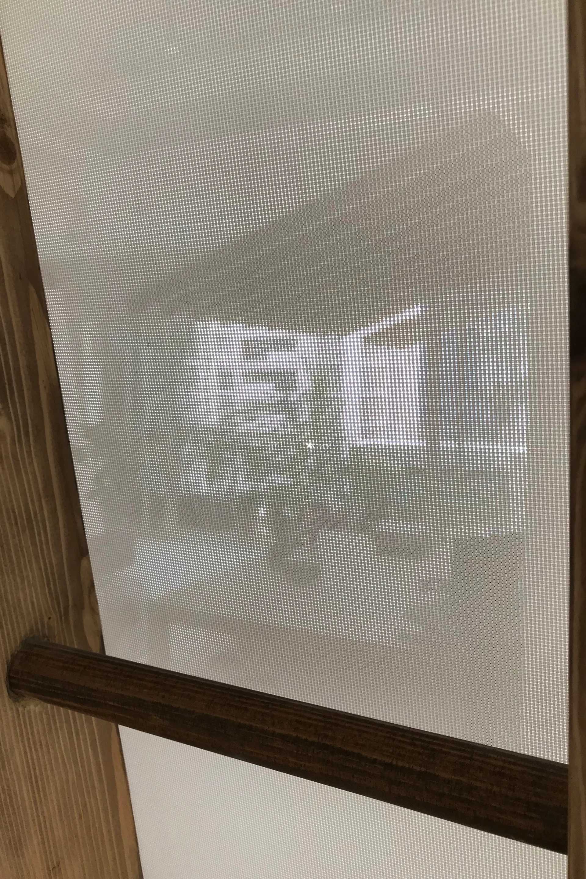 A close-up of a backlit white woven mesh screen panel set within a natural wood frame with a horizontal divider bar.