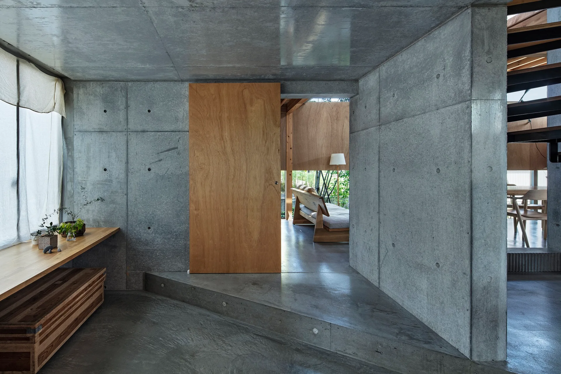 An industrial interior featuring raw exposed concrete walls and floors contrasted by a large natural wood sliding door and built-in desk.