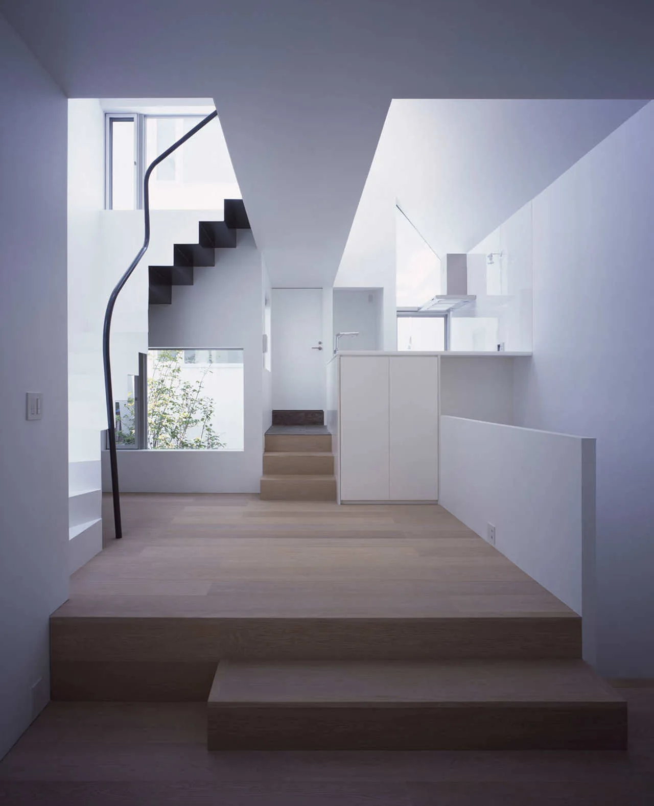 A minimalist split-level residential interior featuring light wood platform floors, white walls, and a black steel staircase with a curved handrail.