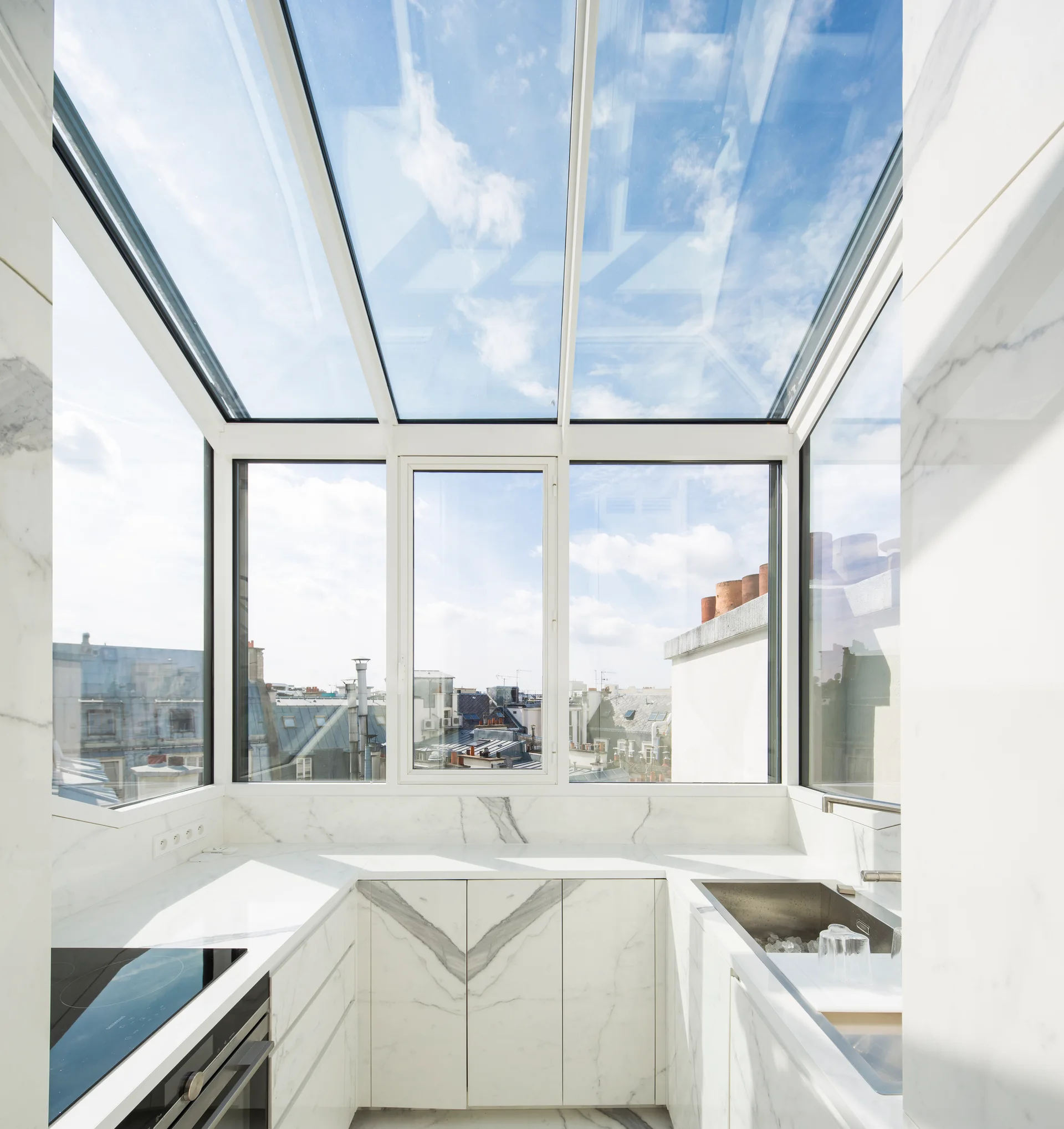 A compact kitchen with veined white marble countertops, matching cabinet fronts, and a large glass skylight ceiling.