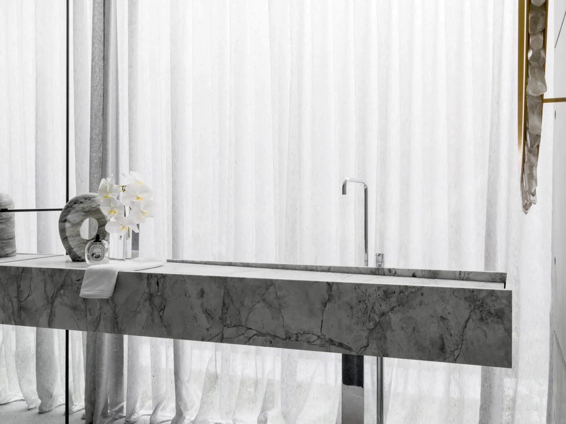 A floating gray marble bathroom vanity with an integrated sink and chrome faucet is set against floor-to-ceiling sheer white curtains.