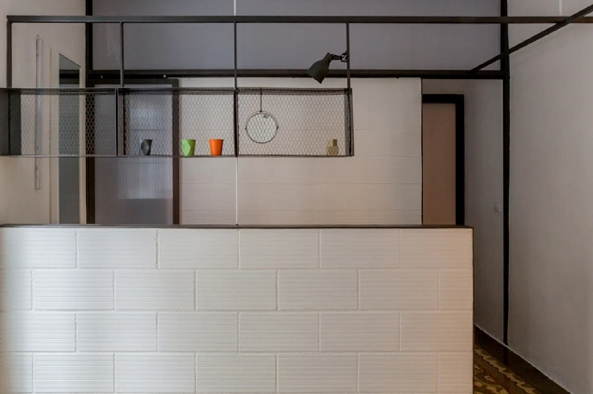 A low white brick partition wall sits below a suspended black metal frame with wire mesh shelves in a minimalist space.