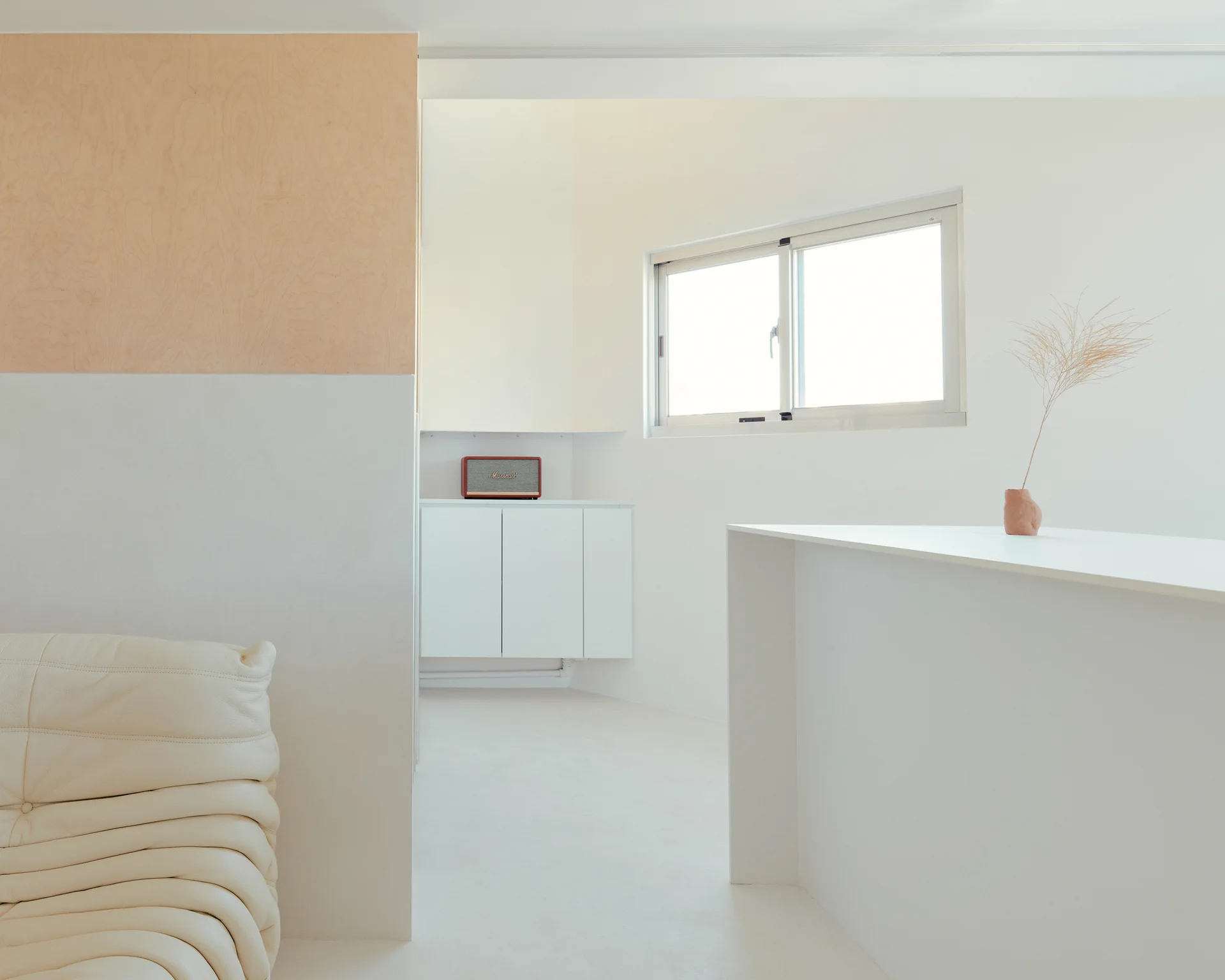 A minimalist white living room with a corner of a cream tufted leather sofa, a light wood wall panel, and a white console cabinet.