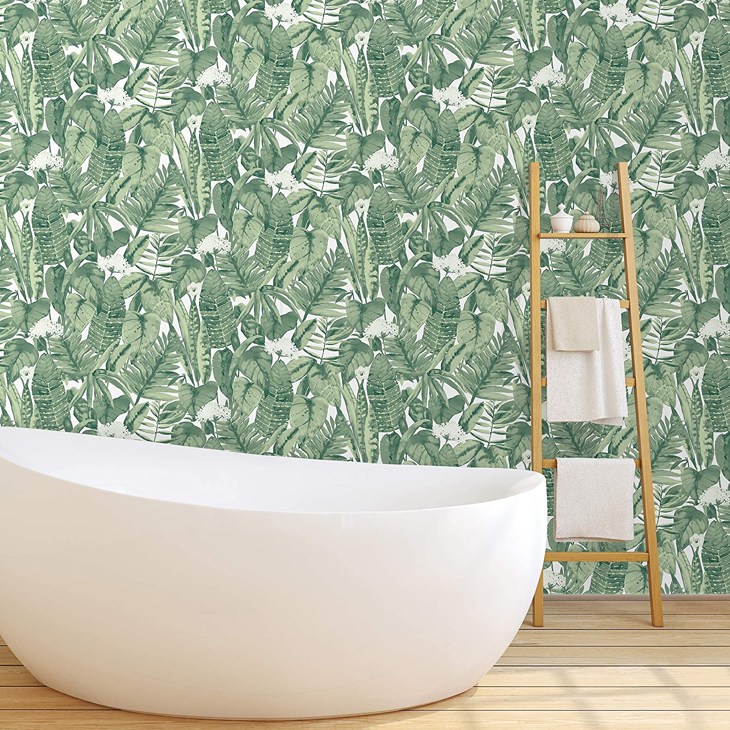 A white freestanding tub sits on light wood flooring in front of green tropical leaf wallpaper, next to a wooden towel ladder.