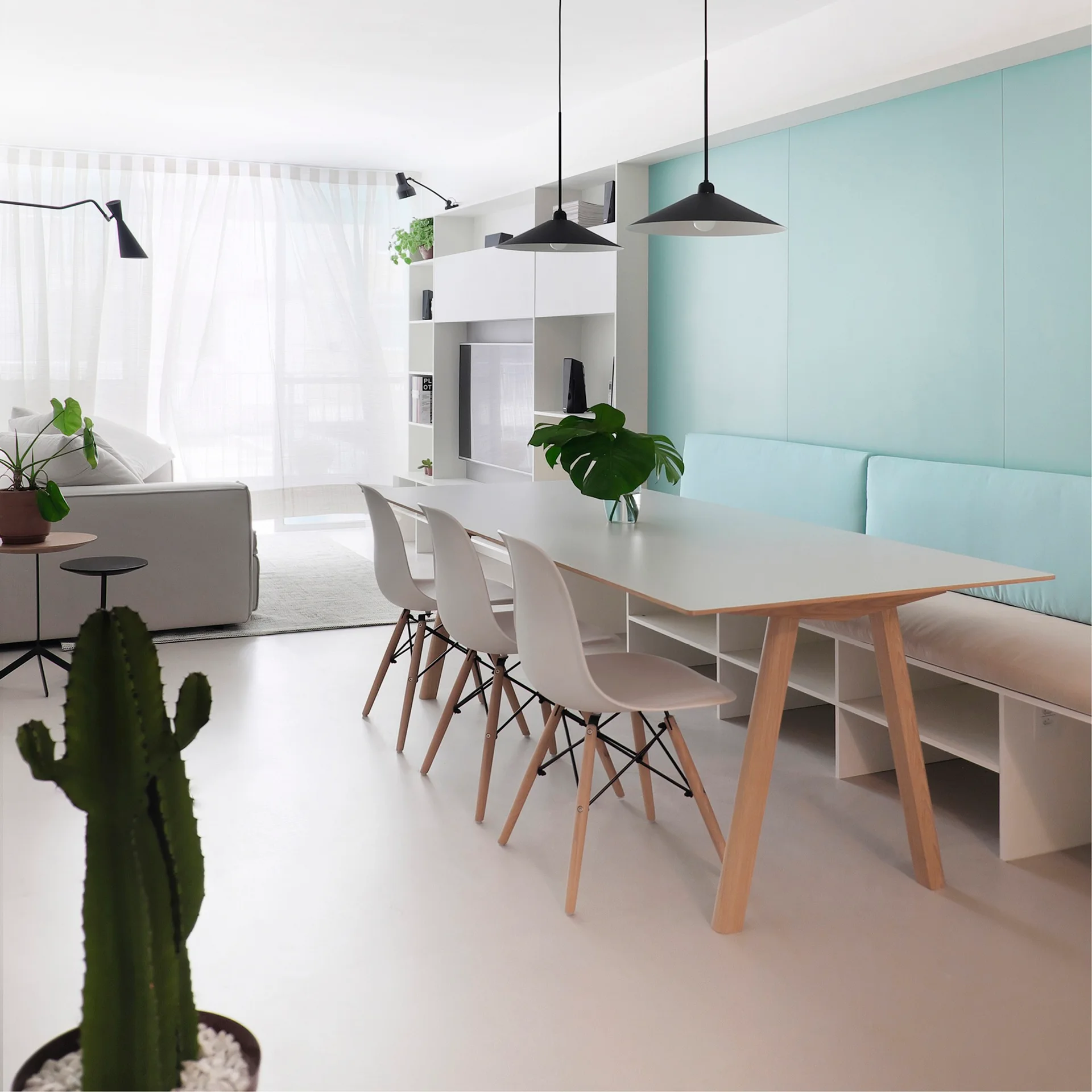 A modern dining room features a white dining table with chairs, a light blue cushioned bench, and sleek black pendant lights.