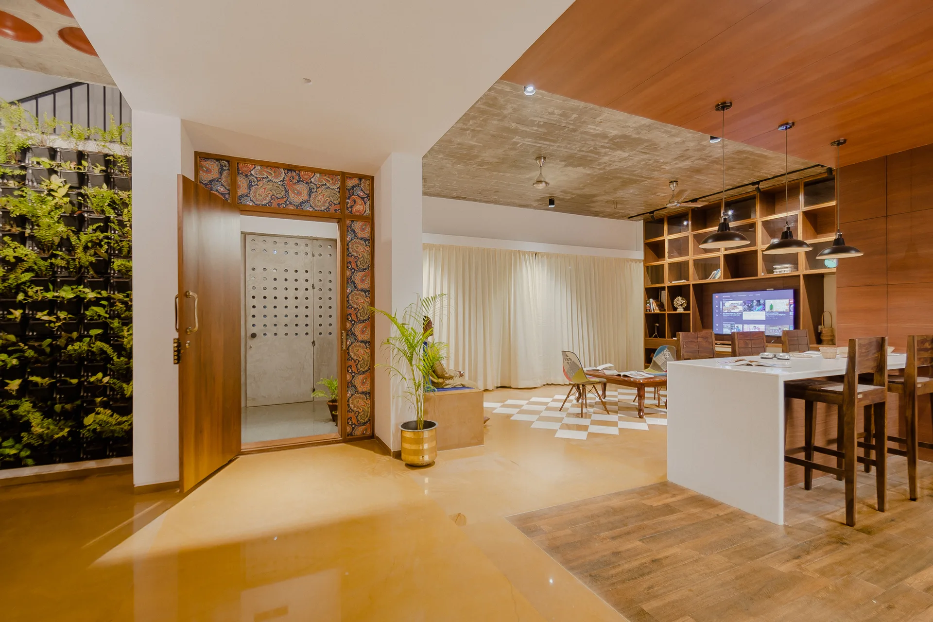 An open-plan residential interior featuring a white kitchen island, an exposed concrete ceiling, wood paneling, and a green vertical garden wall.