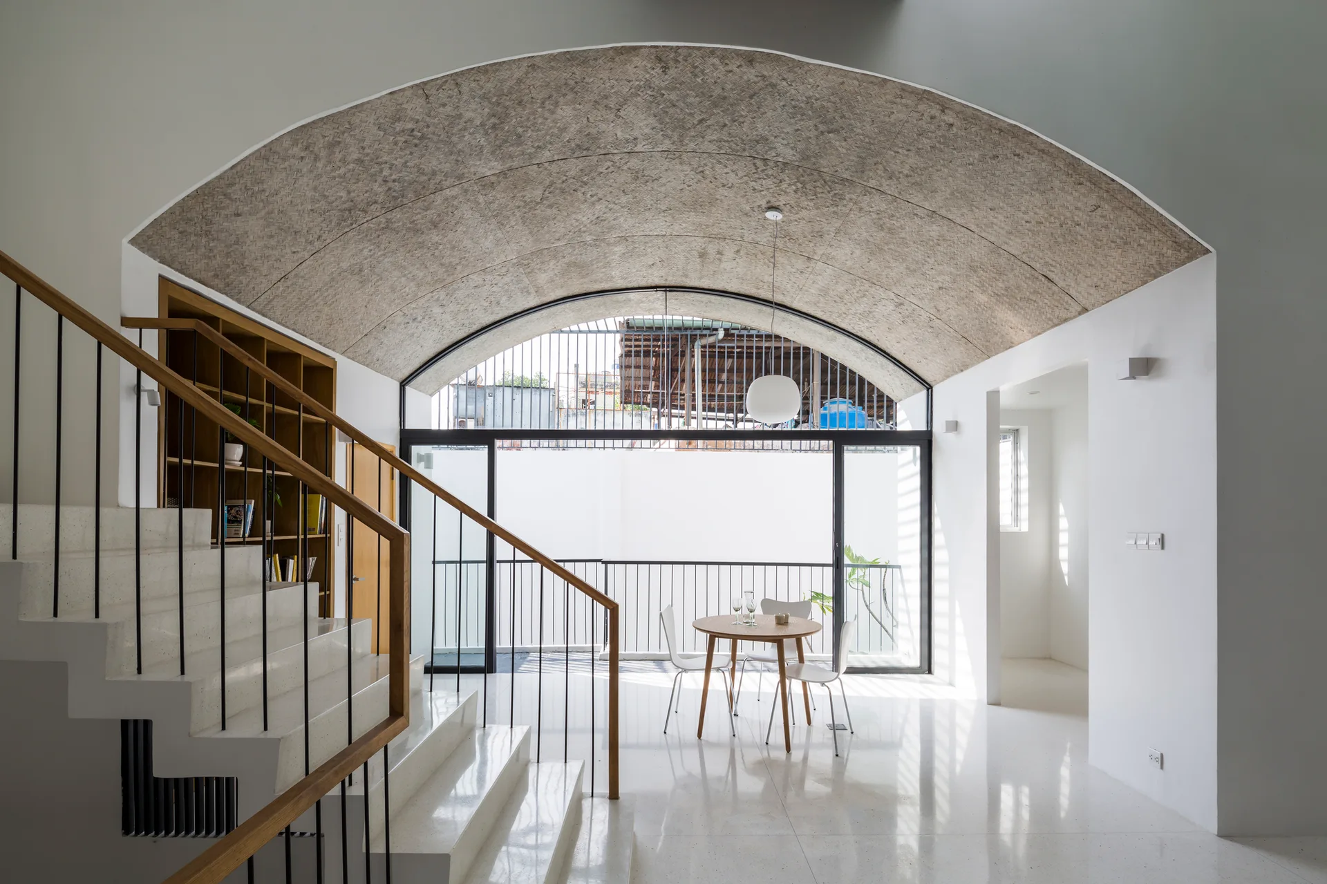 A white interior space featuring a stone staircase, a small round table, and a large arched ceiling covered in textured woven material.