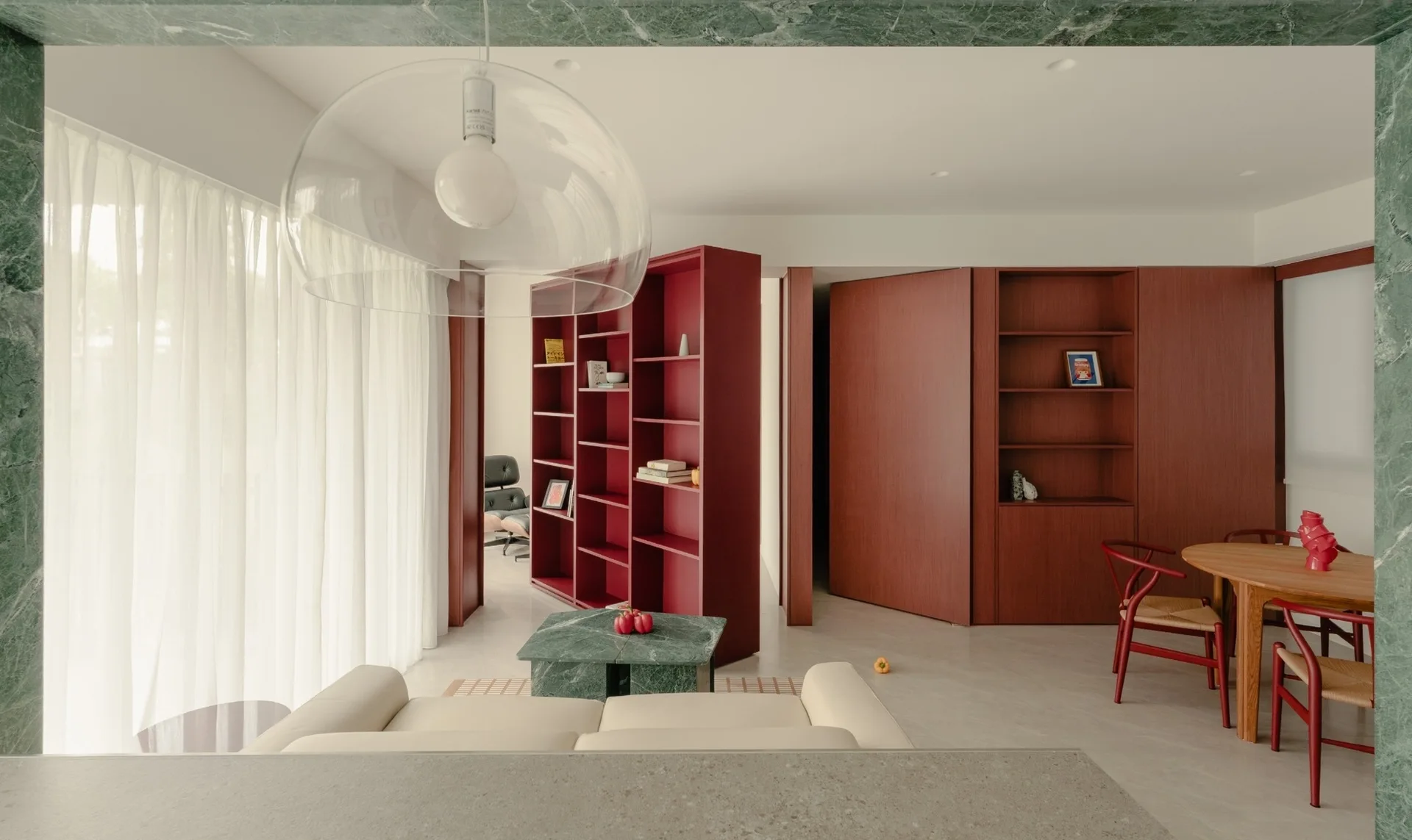 A modern open-plan living and dining space featuring a cream sofa, a green marble coffee table, and custom red wood shelving units.